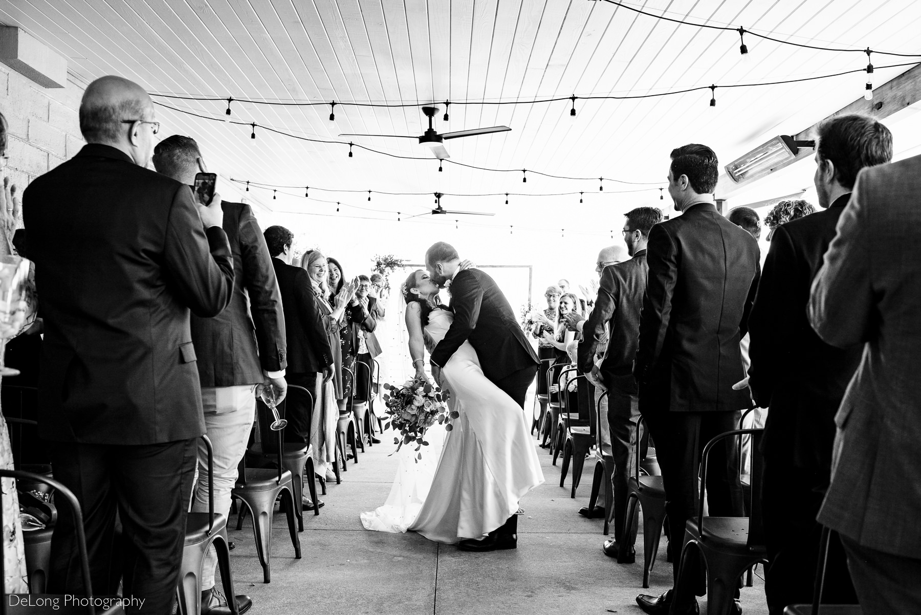 Black and white photograph of groom dipping bridge partway down the aisle after their wedding ceremony. Photograph by Charlotte wedding photographers DeLong Photography.