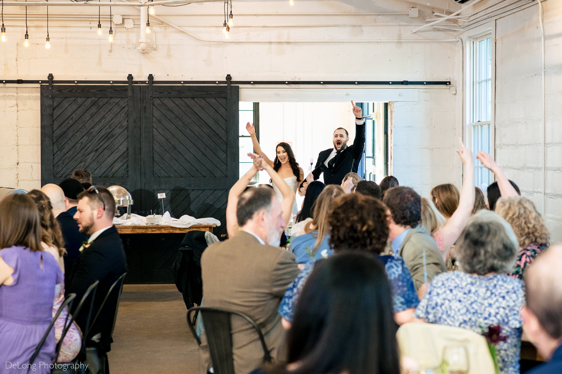 Bride and groom entering their wedding reception with their hands in the air excitedly. Photograph by Charlotte wedding photographers DeLong Photography.