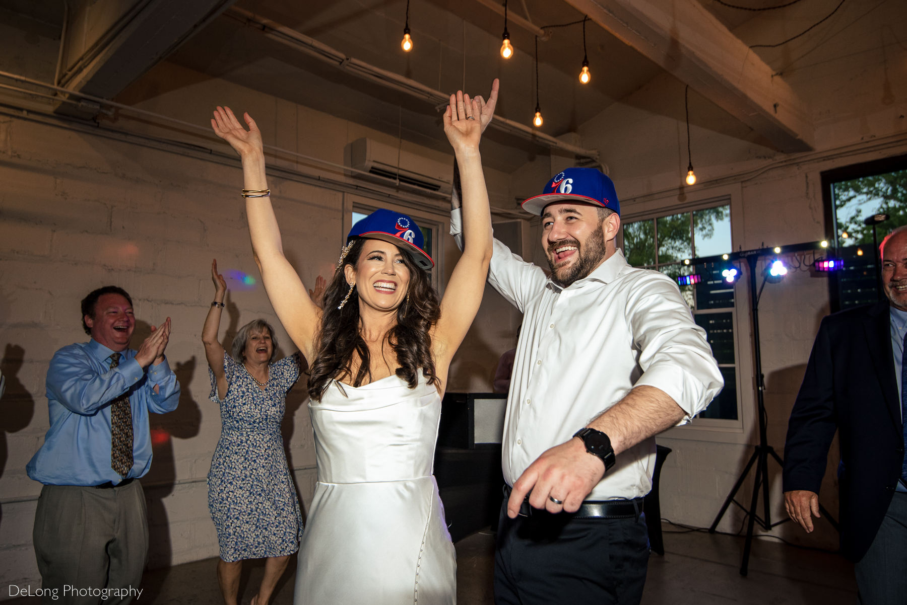 bridge and groom dancing and laughing on the dance floor wearing baseball hats of their favorite team. Photograph by Charlotte wedding photographers DeLong Photography.