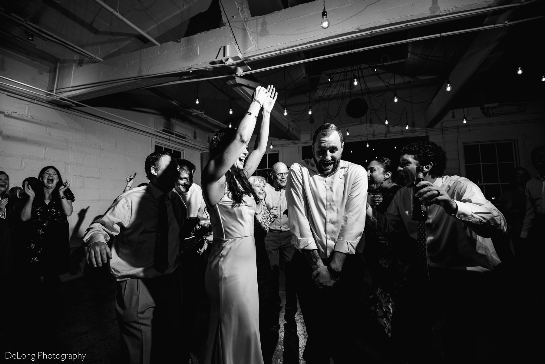 Black and white photograph of a groom reacting as the entire dance floor encircles him tightly. Photograph by Charlotte wedding photographers DeLong Photography.