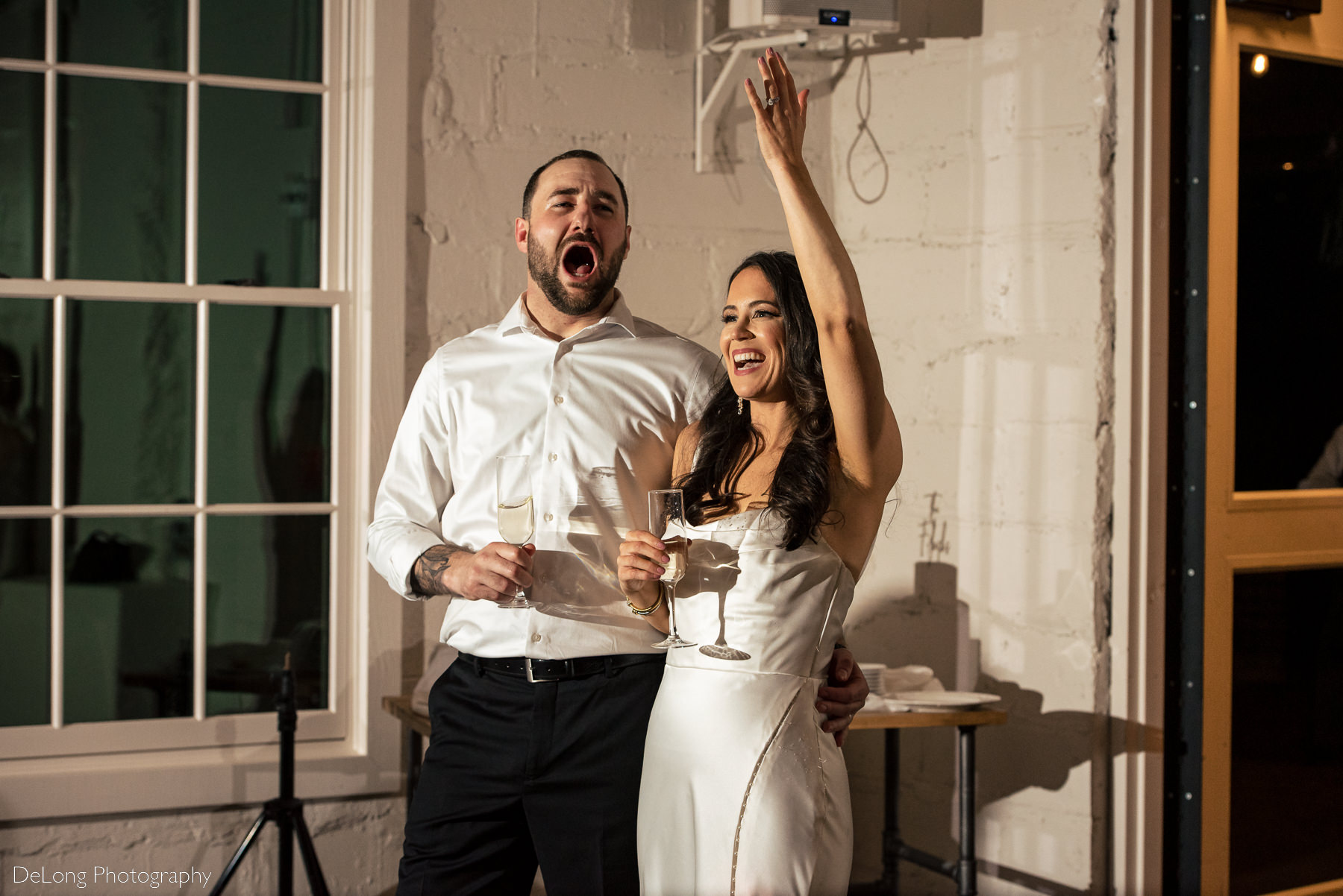 Bride and groom reacting with smiles and cheers during the matron of honor's toast at Upstairs Atlanta. Photograph by Charlotte wedding photographers DeLong Photography.