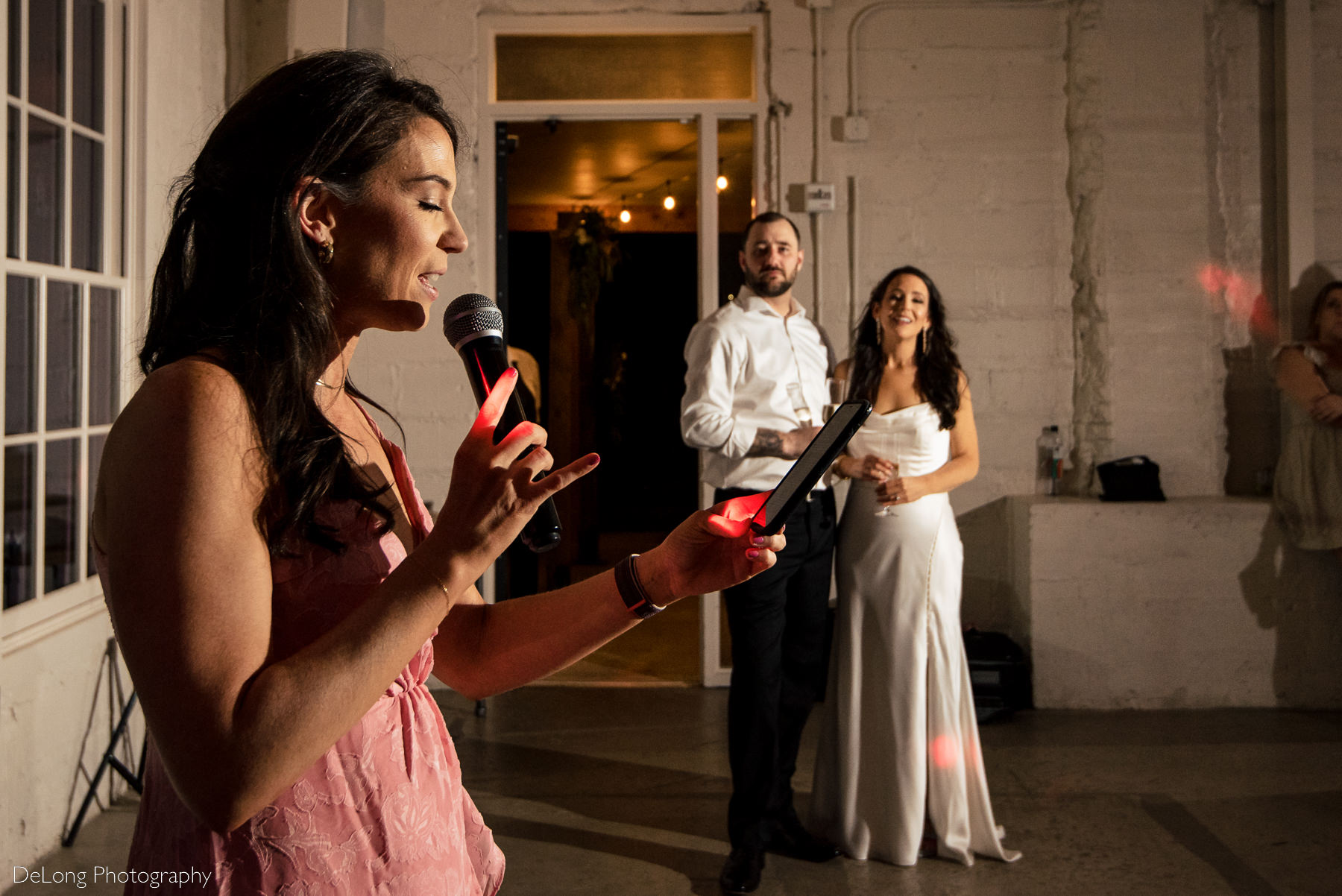 Matron of honor giving a toast while the bride and groom look on in the background. Photograph by Charlotte wedding photographers DeLong Photography.