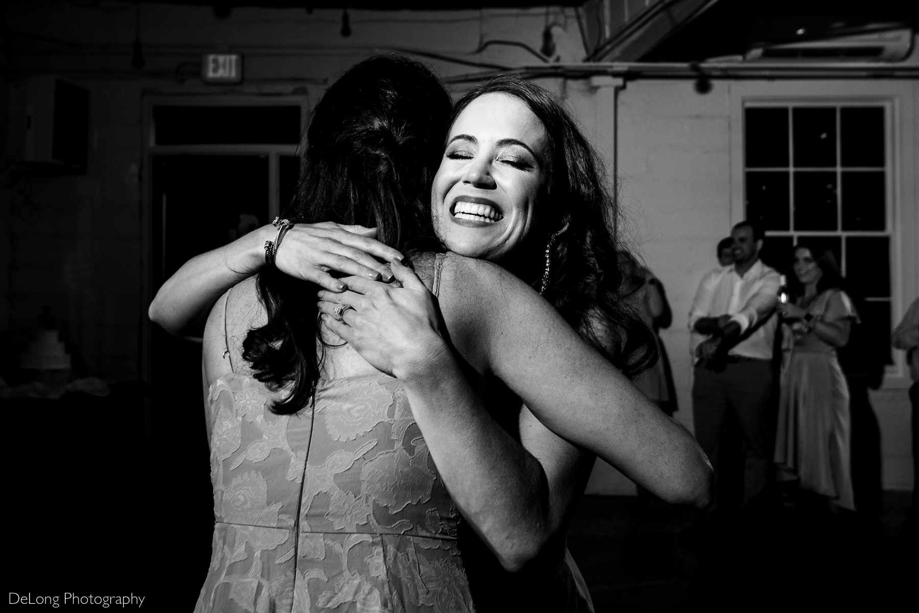 Black and white photograph of the bride beaming with joy and hugging her sister after the matron of honor toast at Upstairs Atlanta. Photograph by Charlotte wedding photographers DeLong Photography.  