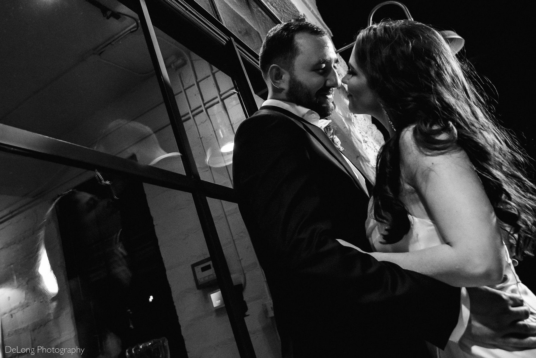 Black and white photograph of a bridge and groom leaned up against the glass windows of Upstairs Atlanta, looking at each other lovingly. Photograph by Charlotte wedding photographers DeLong Photography.