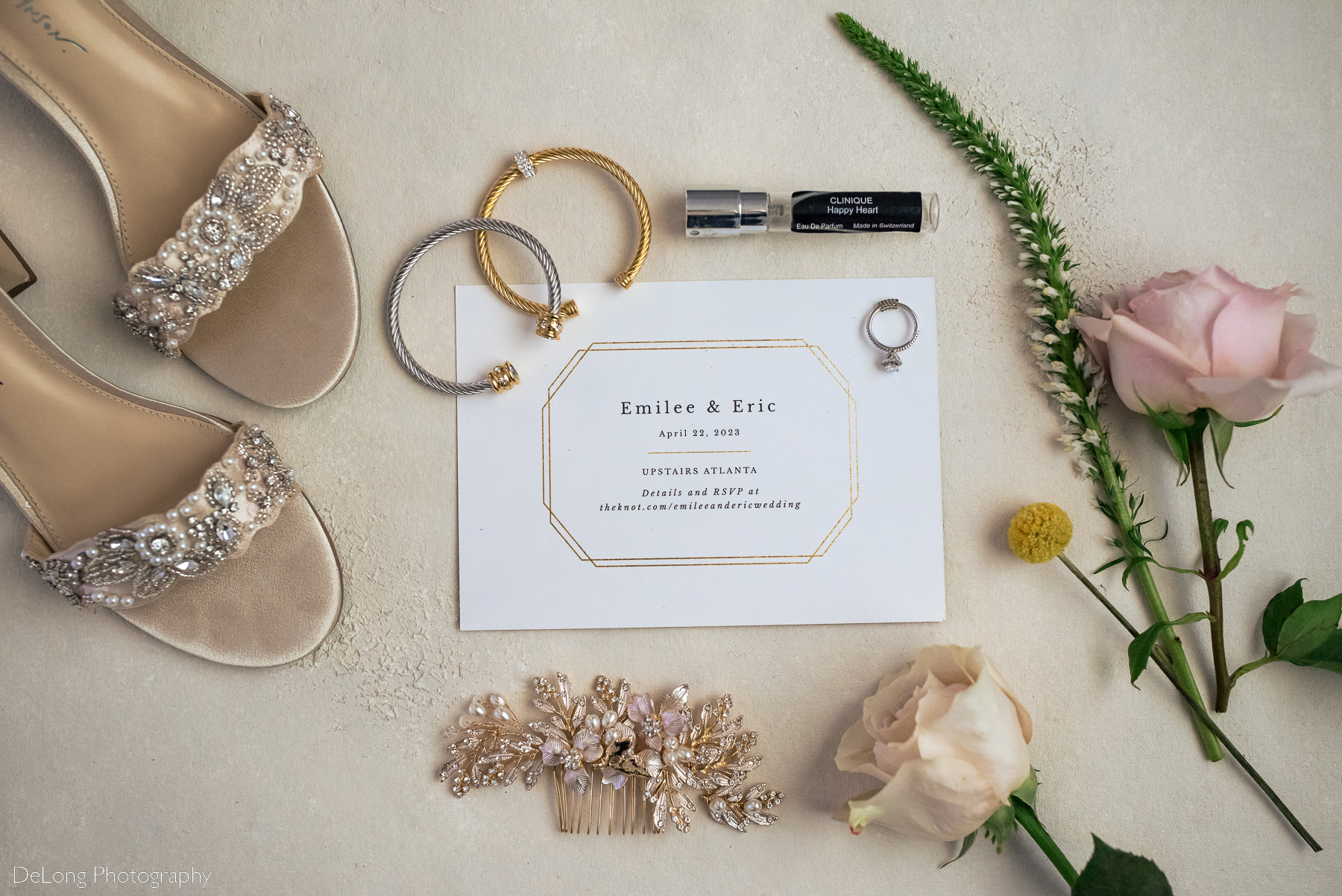 Flat lay of wedding stationary along with jewelry perfume shoes and a jeweled hairpin by Charlotte wedding photographers DeLong Photography