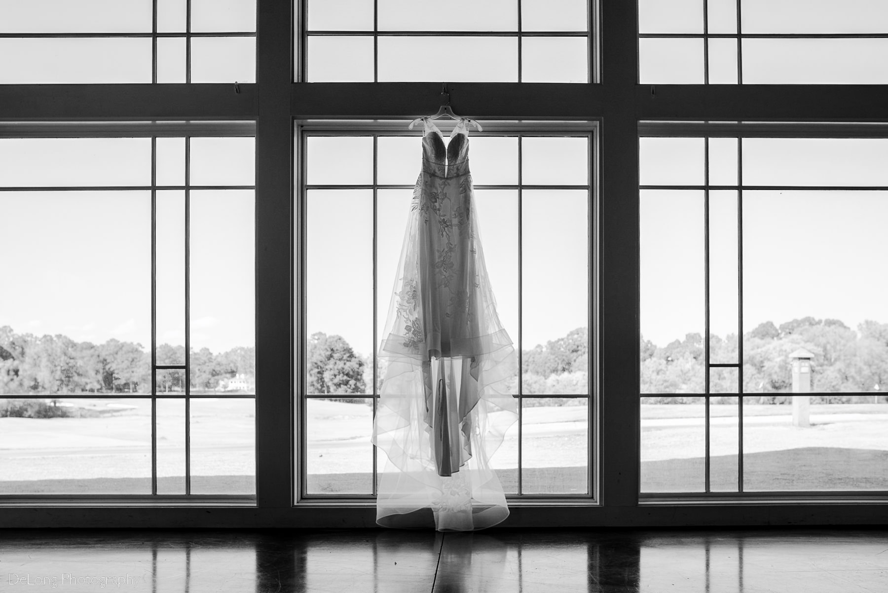 Black and white photograph of wedding dress hanging in the reception space at Pine Island Country Club in Charlotte, NC by Charlotte wedding Photographers DeLong Photography