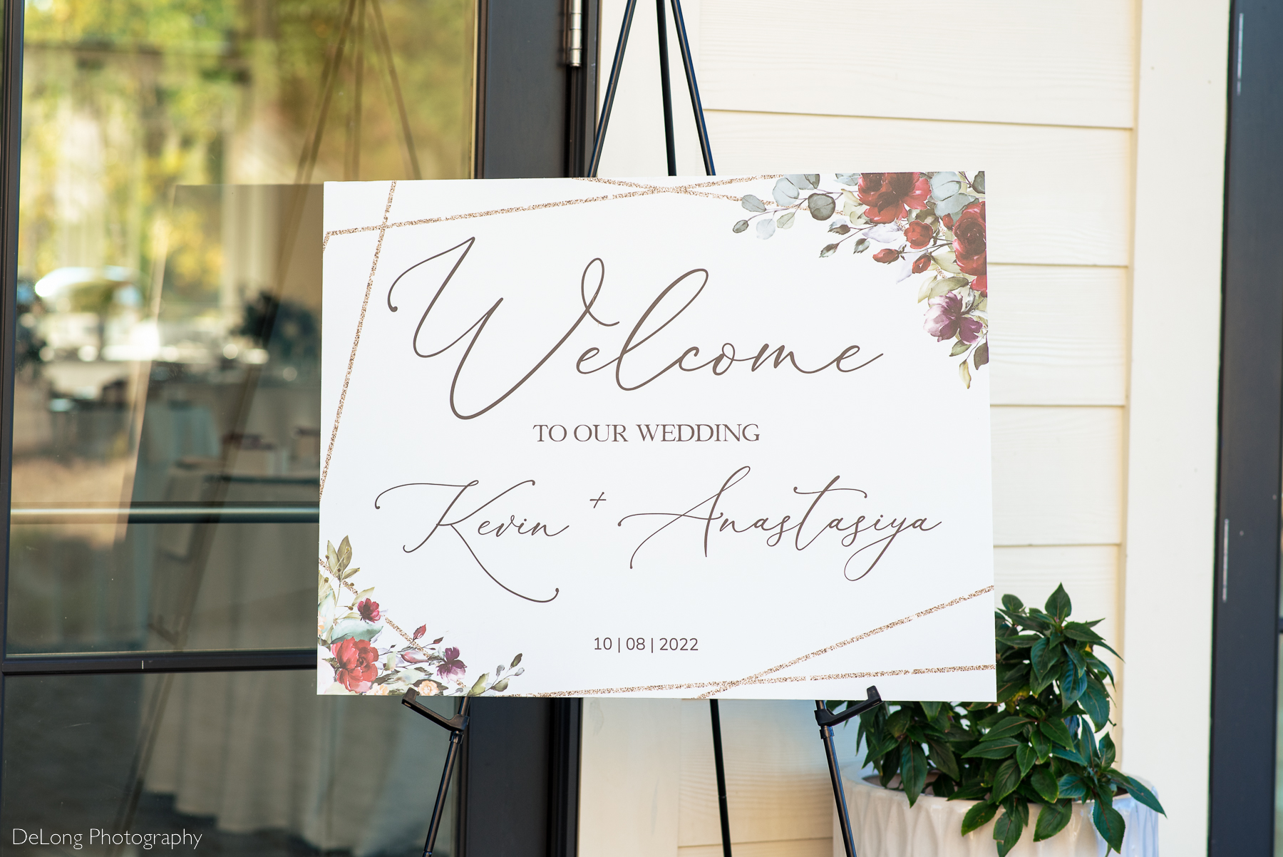 Wedding welcome sign with cursive lettering with red, burgundy, purple, and green florals by Charlotte wedding photographers DeLong Photography
