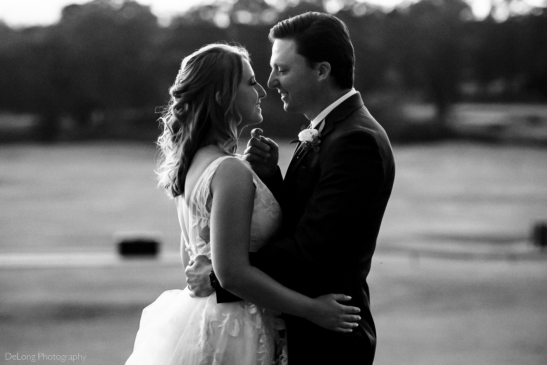 Black and white photograph of bride and groom smiling just before he lifts her chin with his hand for a kiss at Pine Island Country Club in Charlotte, NC by Charlotte wedding Photographers DeLong Photography
