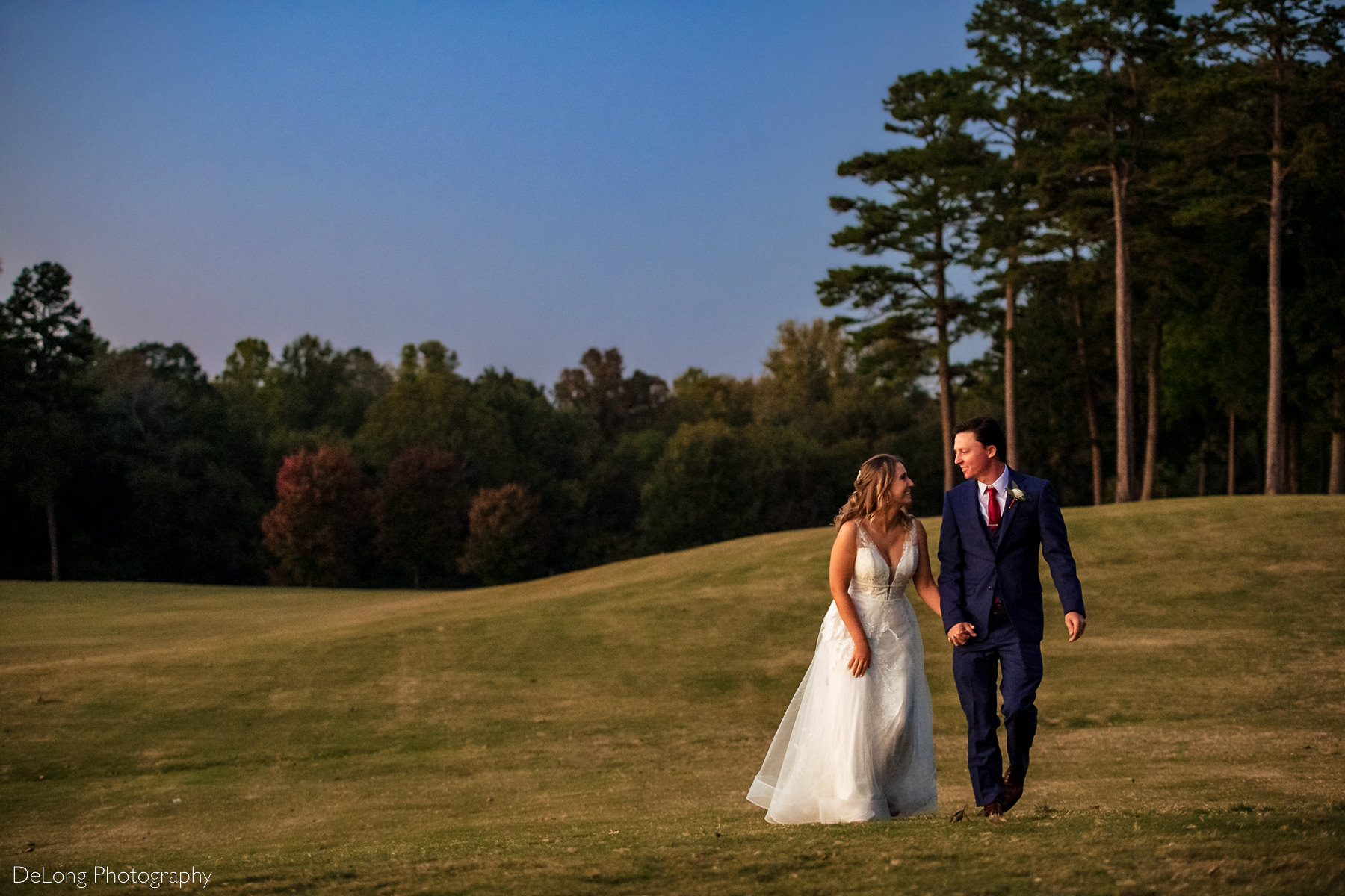 Bride and groom walking toward the camera smiling at one another on the golf course of Pine Island Country Club in Charlotte, NC by Charlotte wedding Photographers DeLong Photography