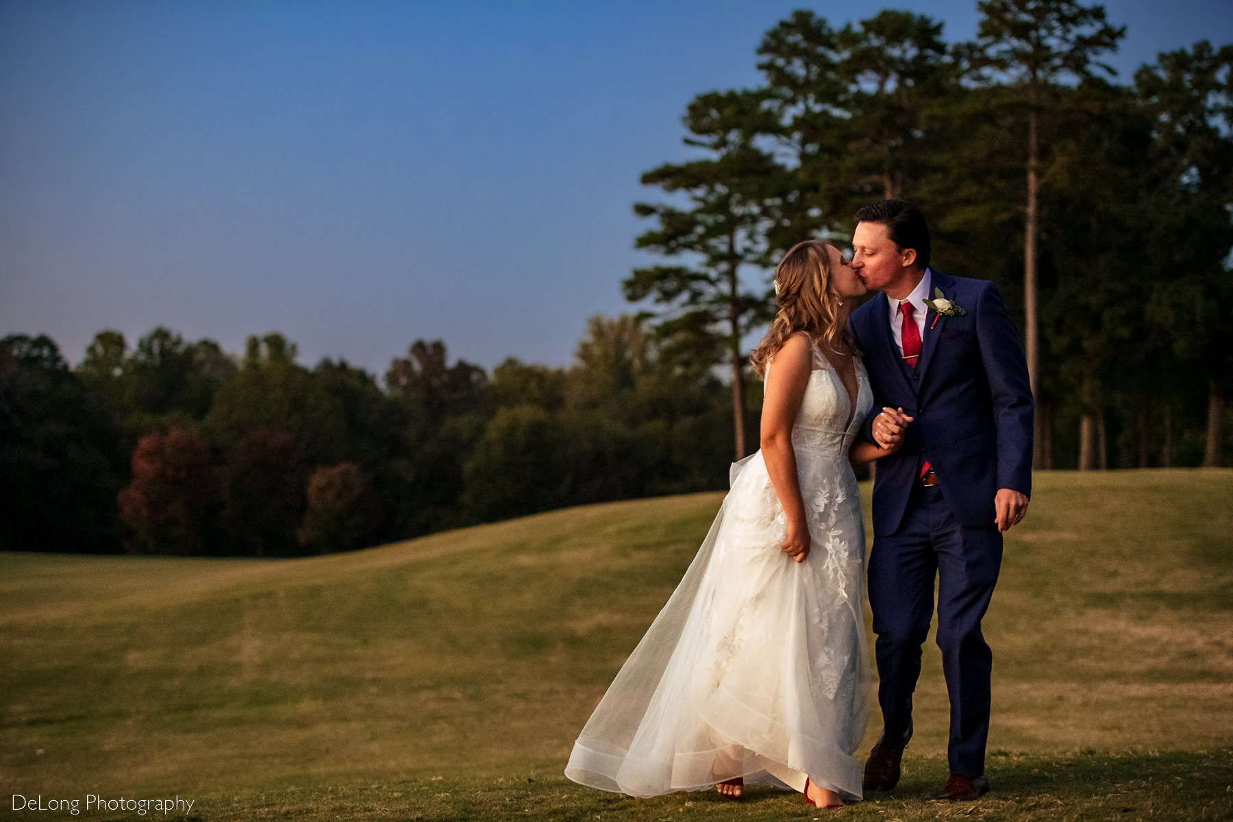 Bride and groom come in for a kiss while walking on the golf course of Pine Island Country Club in Charlotte, NC by Charlotte wedding Photographers DeLong Photography