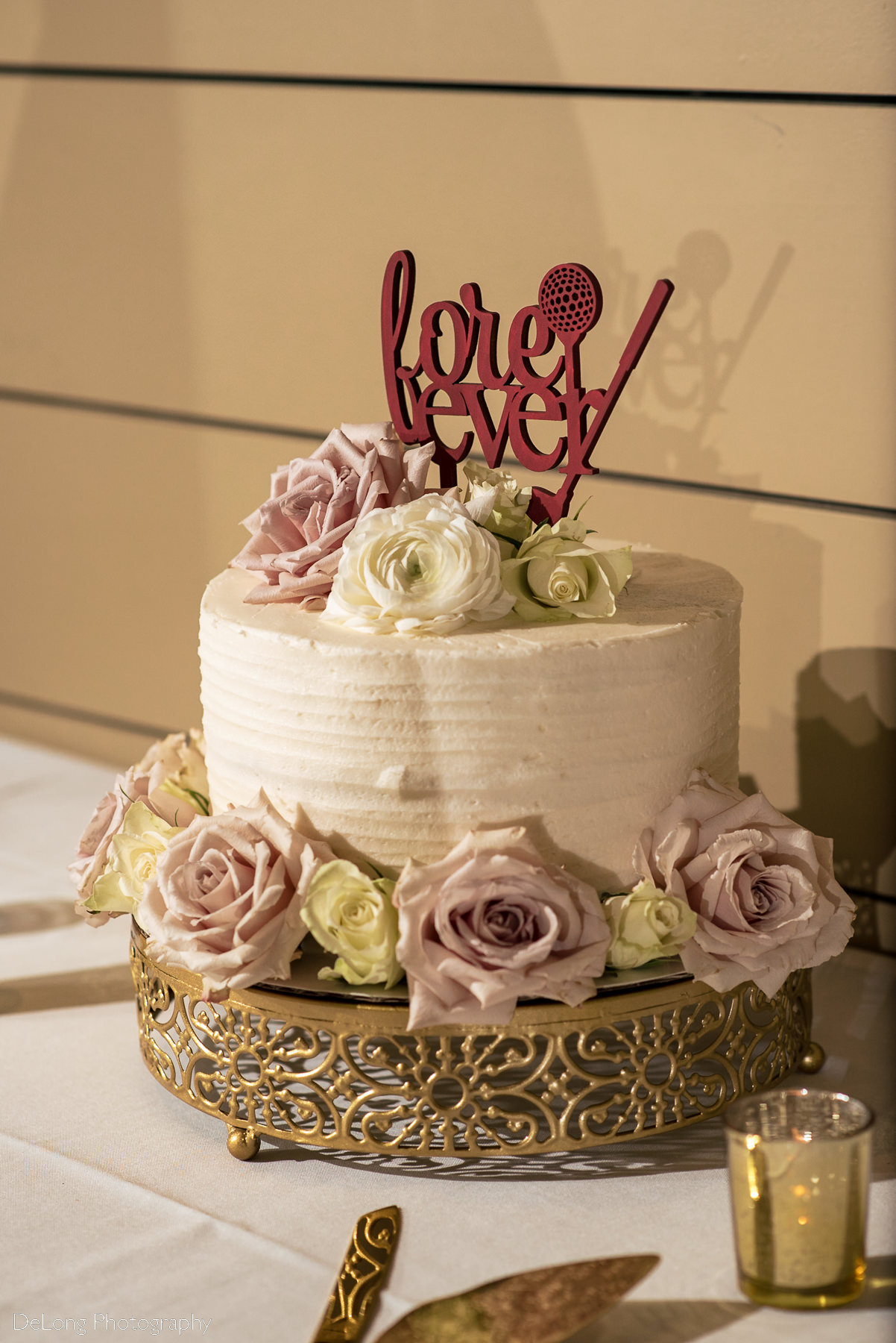 Wedding cake with blush and cream roses and a burgundy cake topper that reads "Fore-ever" with a golf club, ball and tee incorporated into the design by Charlotte wedding Photographers DeLong Photography