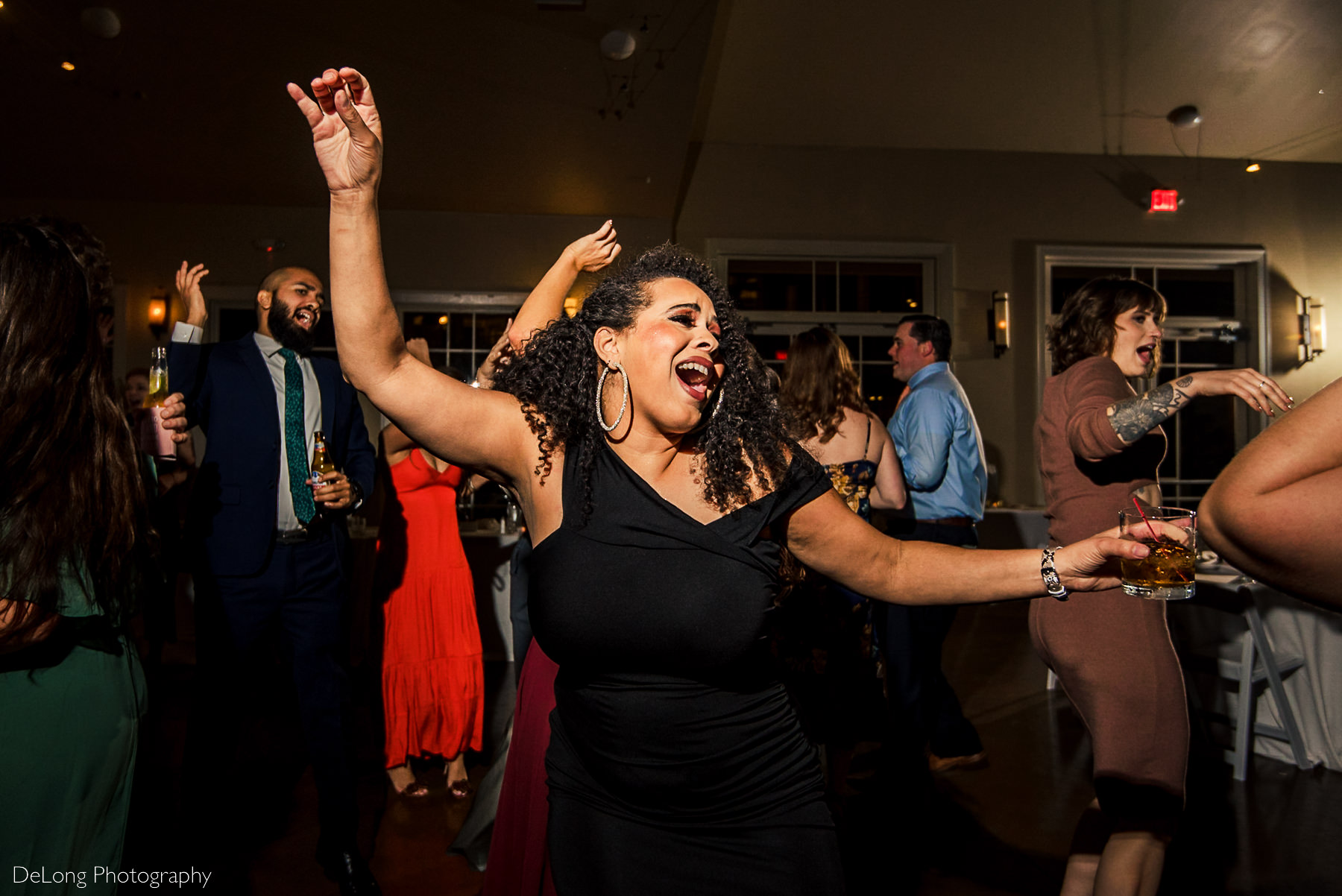 Image of woman holding a cocktail and singing to a song on the dance floor with her hands in the air at Pine Island Country Club in Charlotte, NC by Charlotte wedding Photographers DeLong Photography
