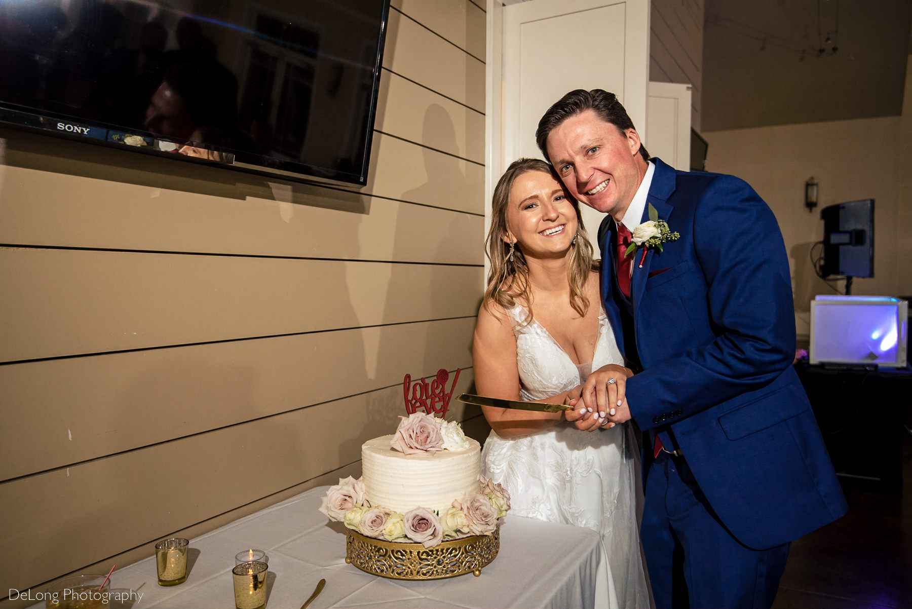 Bride and groom smiling at the camera holding their cake knife before they cut their wedding cake at Pine Island Country Club in Charlotte, NC by Charlotte wedding Photographers DeLong Photography