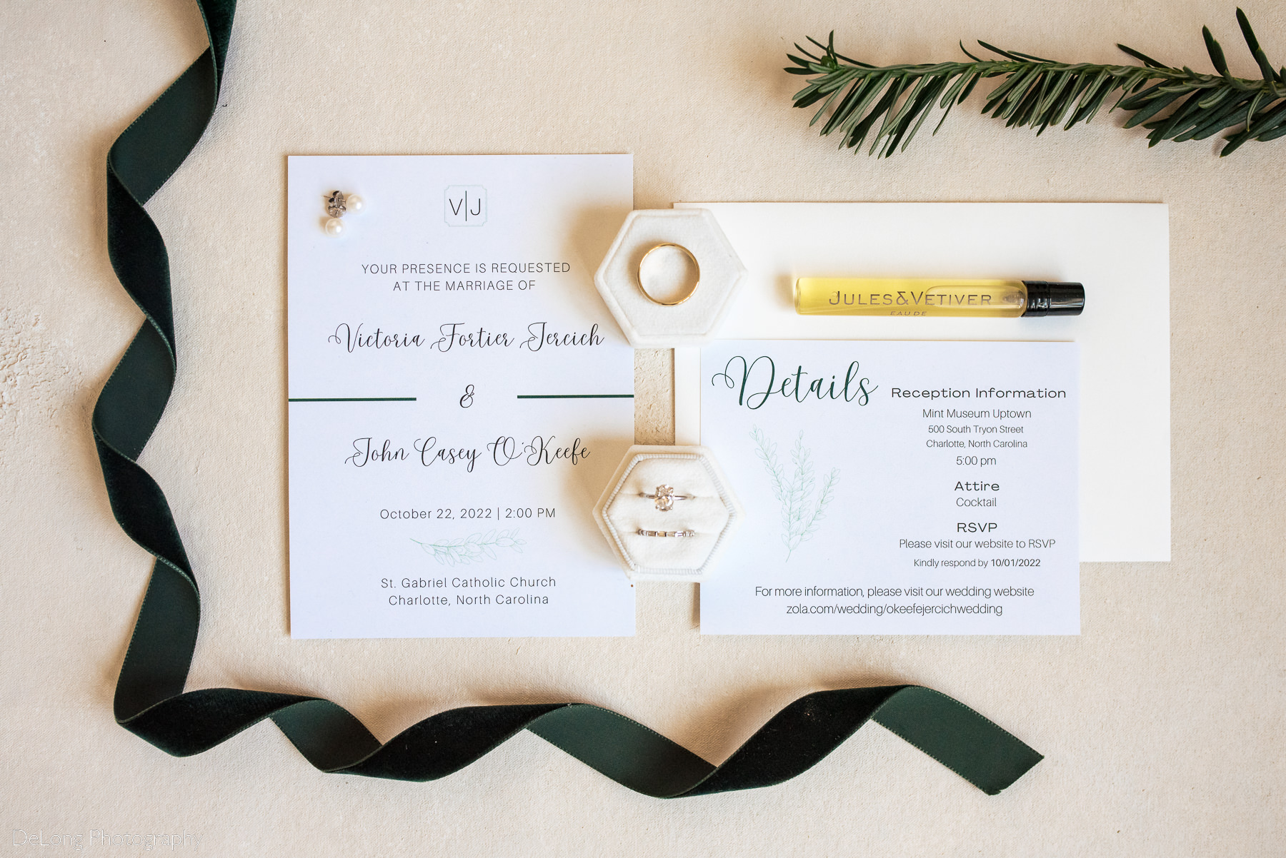 flat lay of wedding stationary along with jewelry perfume and dark green ribbon by Charlotte wedding photographers DeLong Photography