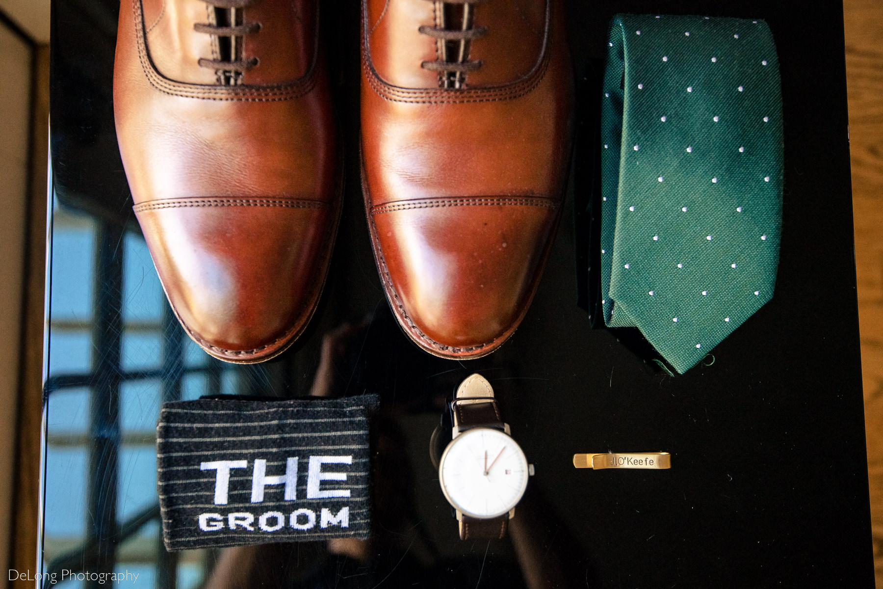 groom's details including brown leather shoes, dark green tie, black and white leather banded watch, engraved tie clip, and "the groom" socks by Charlotte wedding photographers DeLong Photography