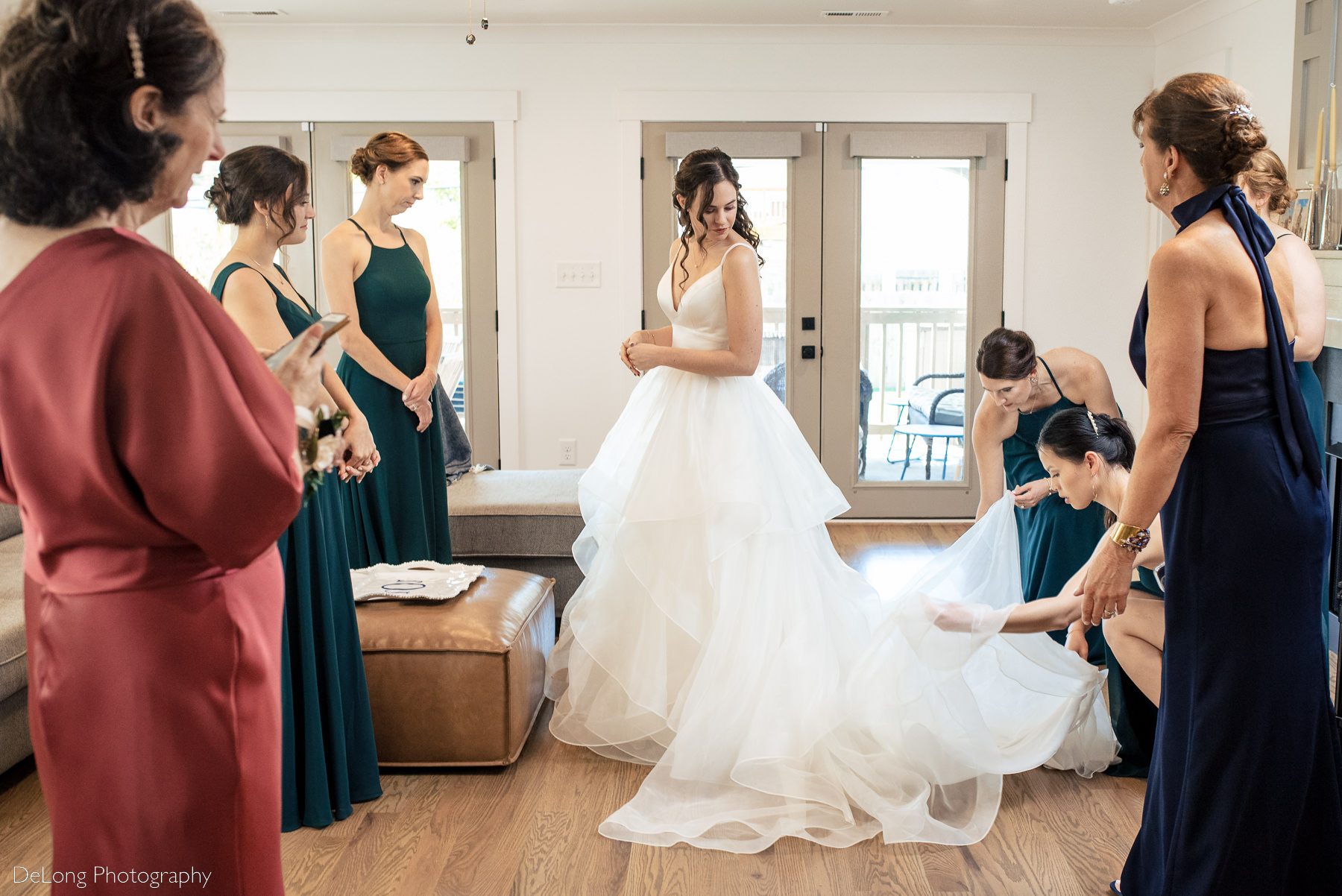 Candid moment of bridesmaids adjusting the bride's dress during getting ready by Charlotte wedding photographers DeLong Photography