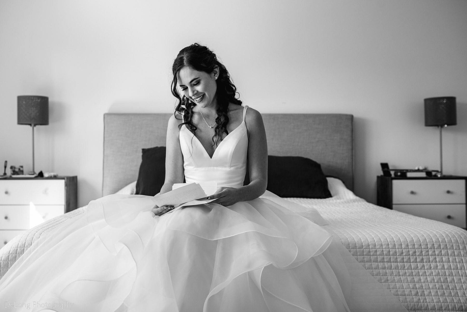 Black and white image of bride smiling while reading a letter from her groom on a bed by Charlotte wedding photographers DeLong Photography