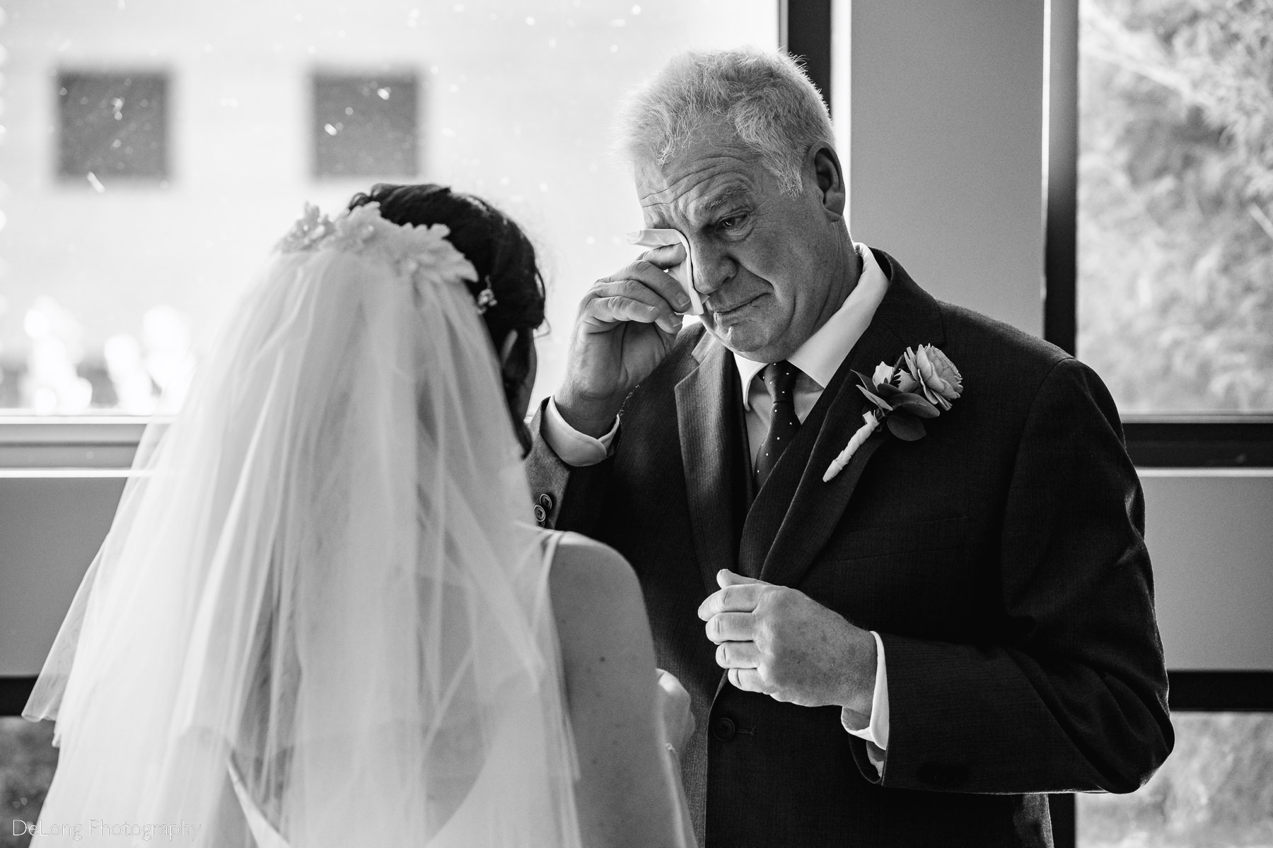 Black and white image of father wiping tears form his eyes during father-daughter first look at St Gabriel Catholic Church in Charlotte, NC by Charlotte wedding photographers DeLong Photography