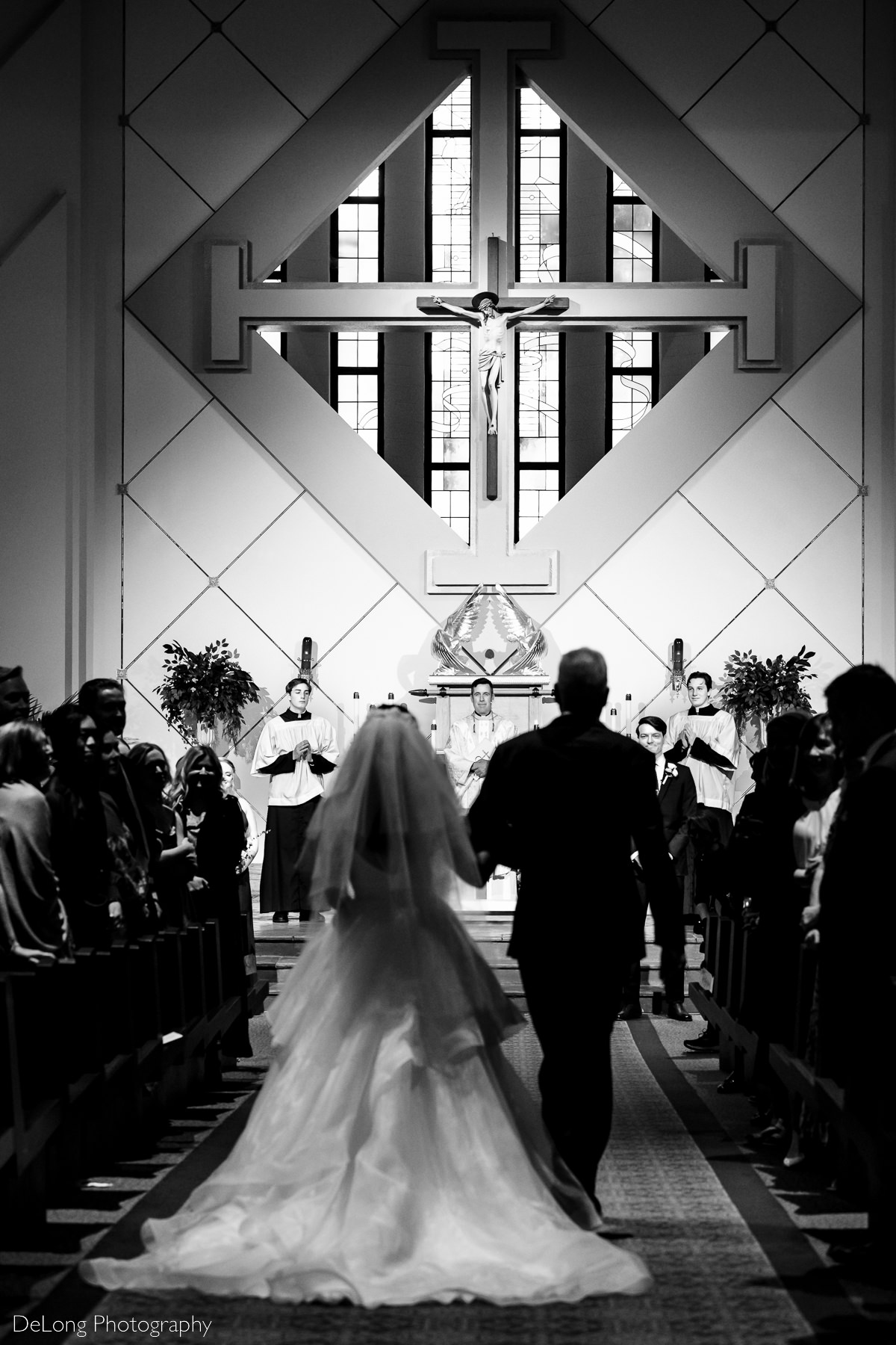 Vertical black and white image of bride walking down the aisle with her father at St Gabriel Catholic Church in Charlotte, NC by Charlotte wedding photographers DeLong Photography