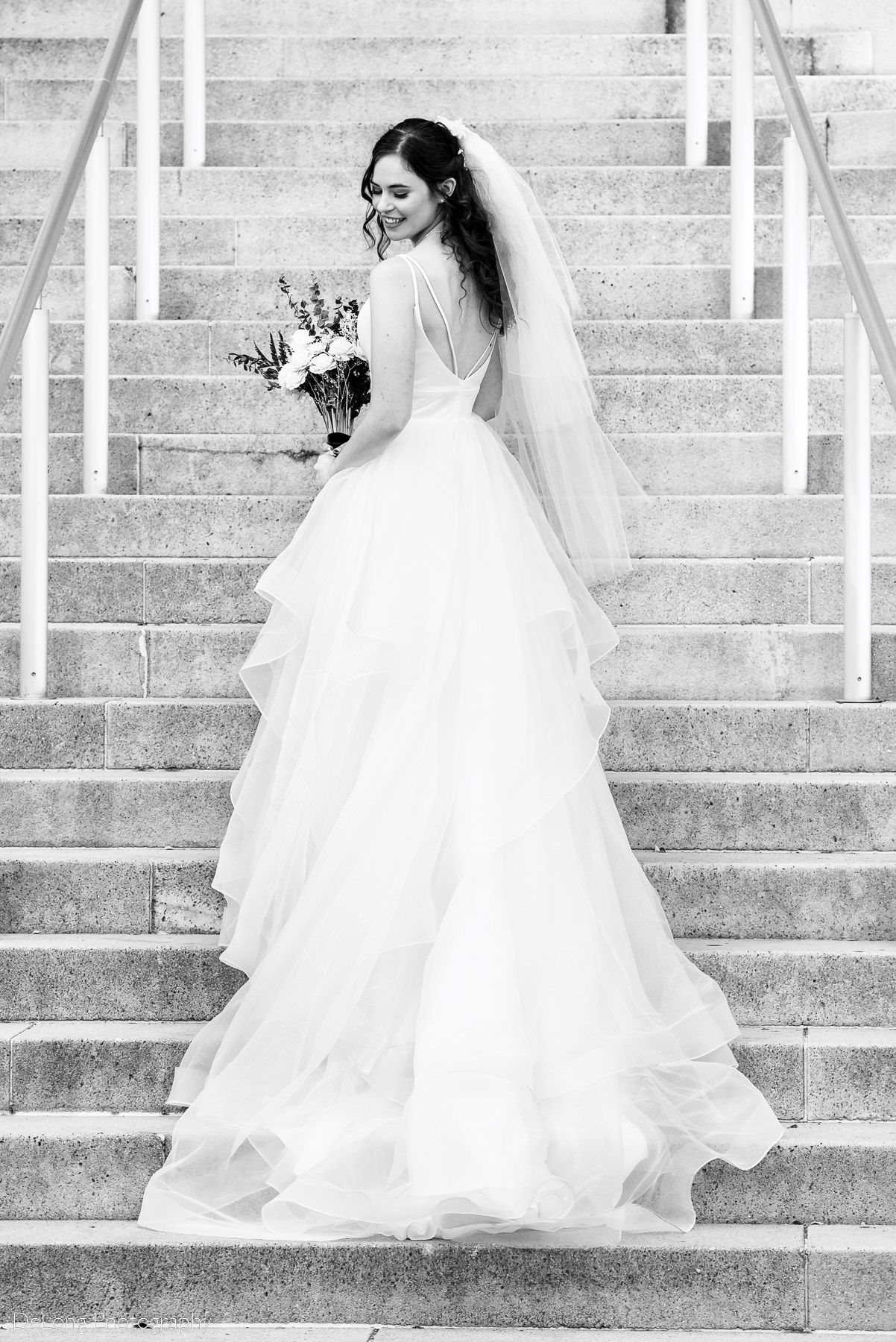 Black and white bridal portrait her facing away and looking back over her shoulder on the steps of the Mint Museum Uptown by Charlotte wedding photographers DeLong Photography
