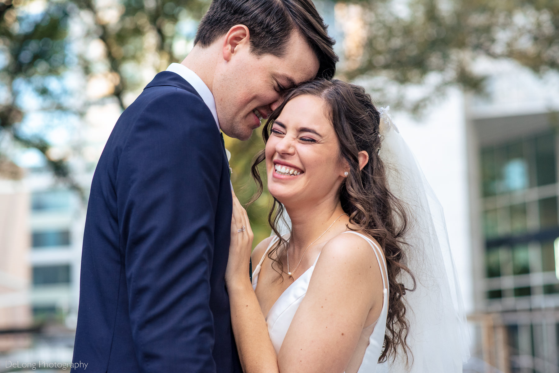 Bride giggling as groom whispers in her ear outside in front of the Mint Museum Uptown by Charlotte wedding photographers DeLong Photography