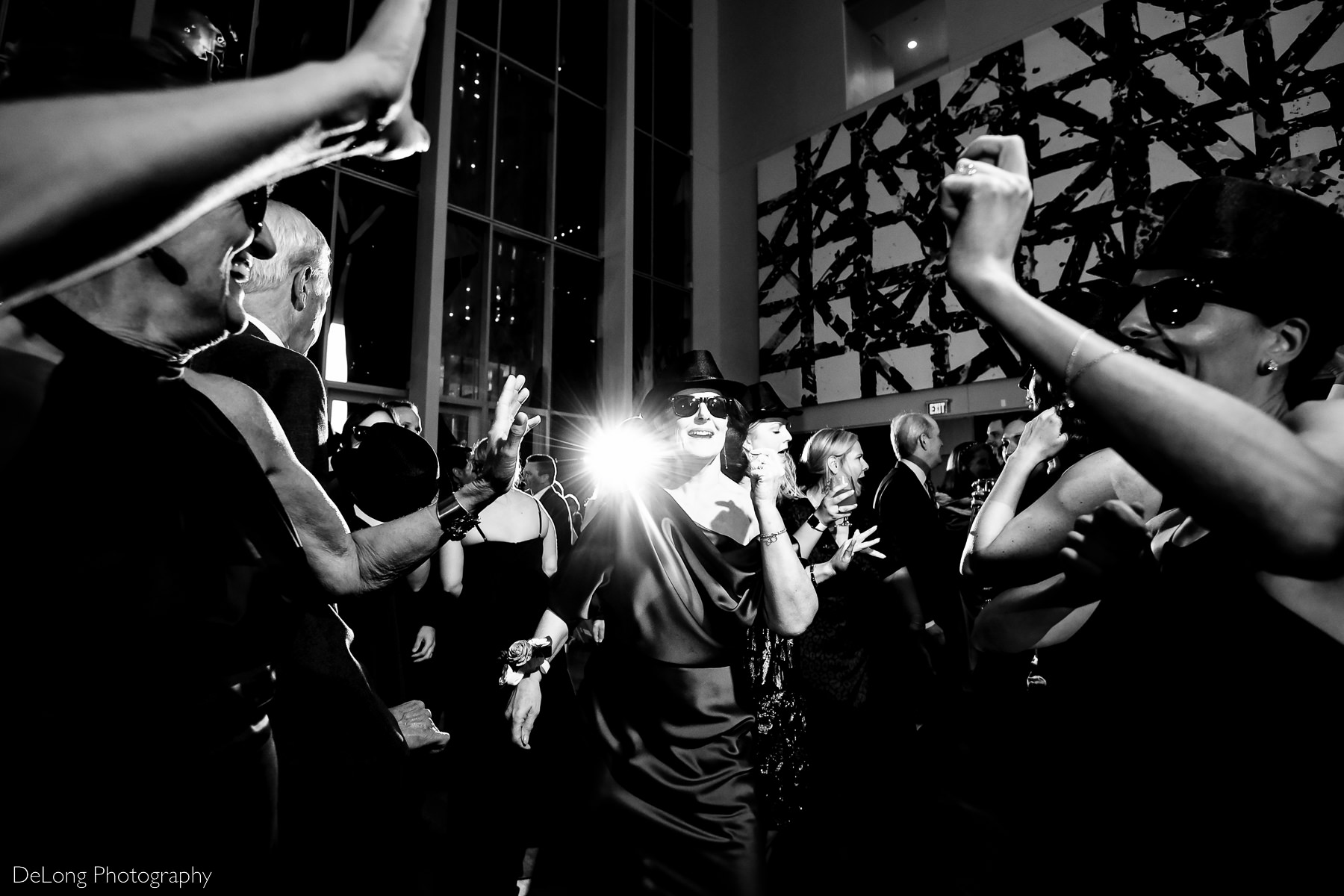Black and white image of guets having fun in sunglasses and top hats on the dance floor of the Mint Museum Uptown by Charlotte wedding photographers DeLong Photography