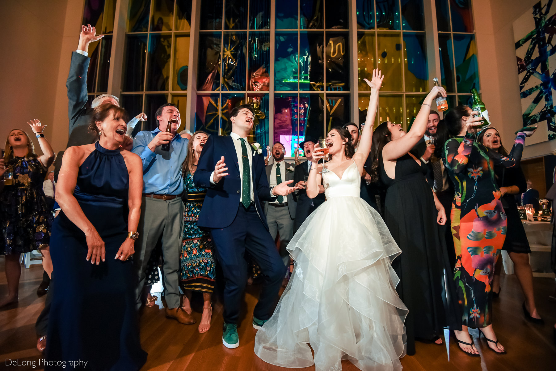 Bride and groom in the center of the crowd of everyone belting lyrics on the dance floor of the Mint Museum Uptown by Charlotte wedding photographers DeLong Photography