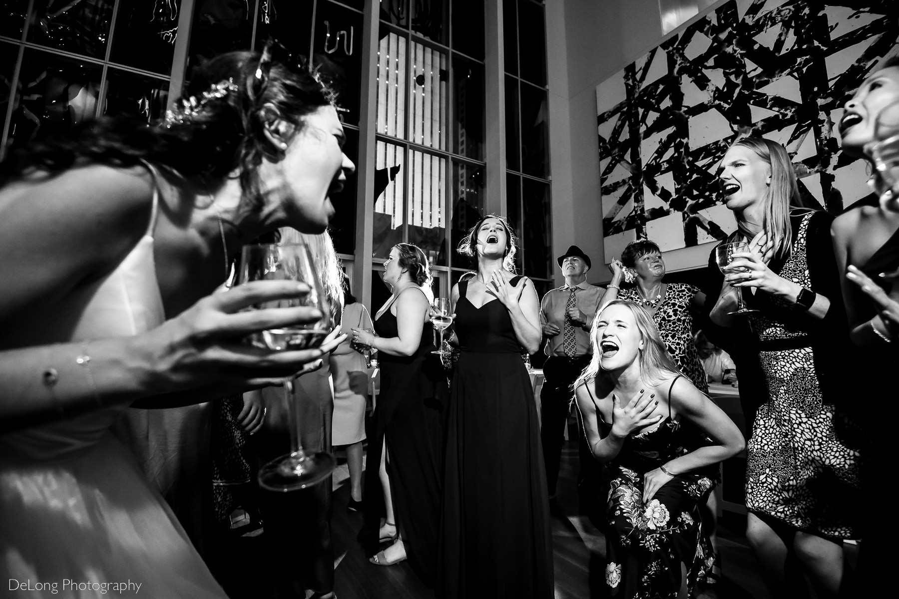 Guest bent over belting lyrics passionately with the bride surrounded by other singing guests on the dance floor of the Mint Museum Uptown by Charlotte wedding photographers DeLong Photography