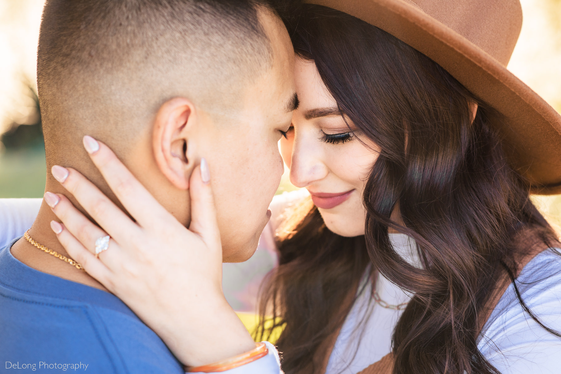 Up-close photograph of couple with their foreheads together, eyes closed, showing the new engagement ring on the woman's hand at Riverfront Park in Columbia, SC. Photo by Charlotte wedding photographers DeLong Photography.