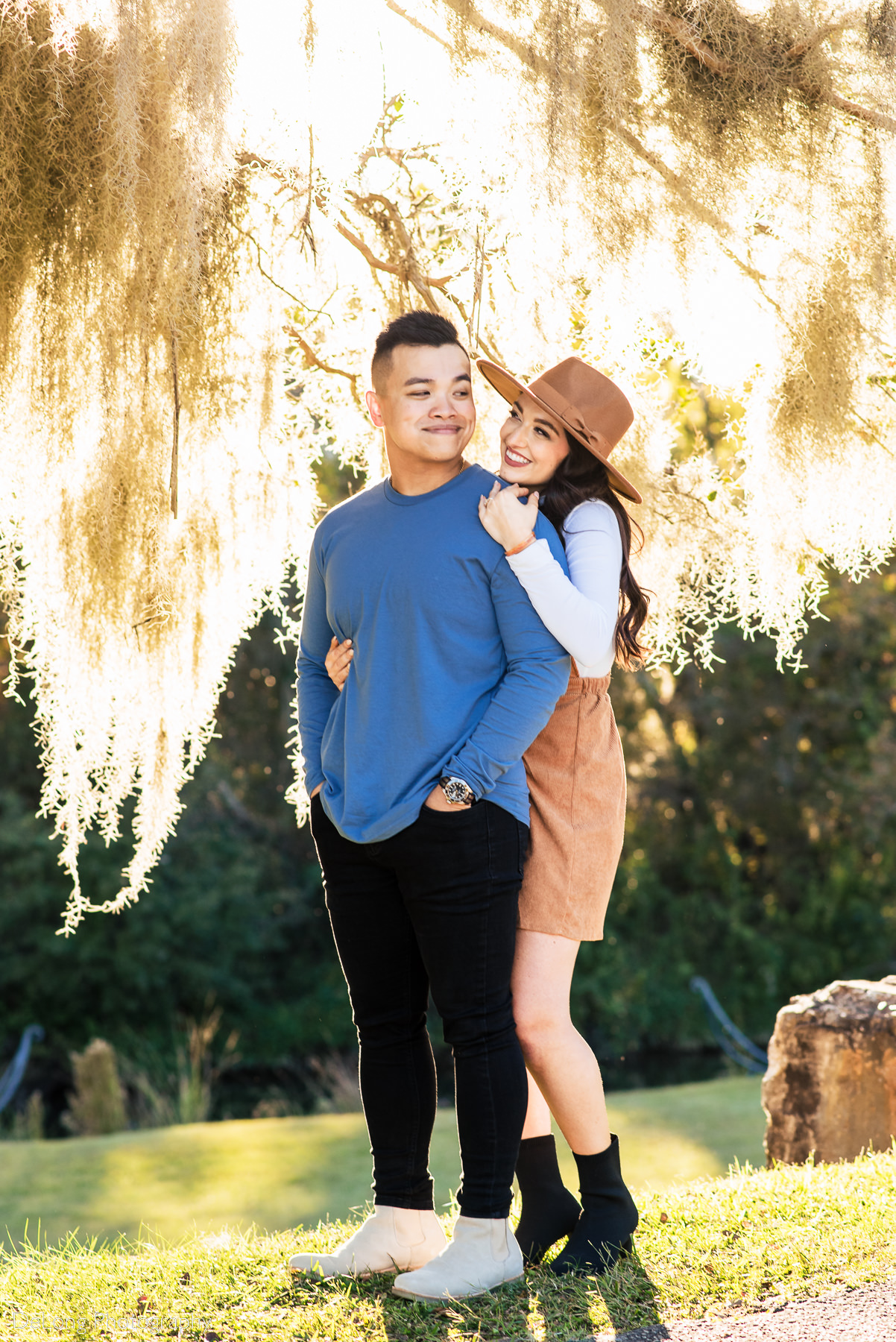 woman snuggling up to her partner beneath the golden mossy trees during the afternoon light at Riverfront Park in Columbia, SC. Photo by Charlotte wedding photographers DeLong Photography.