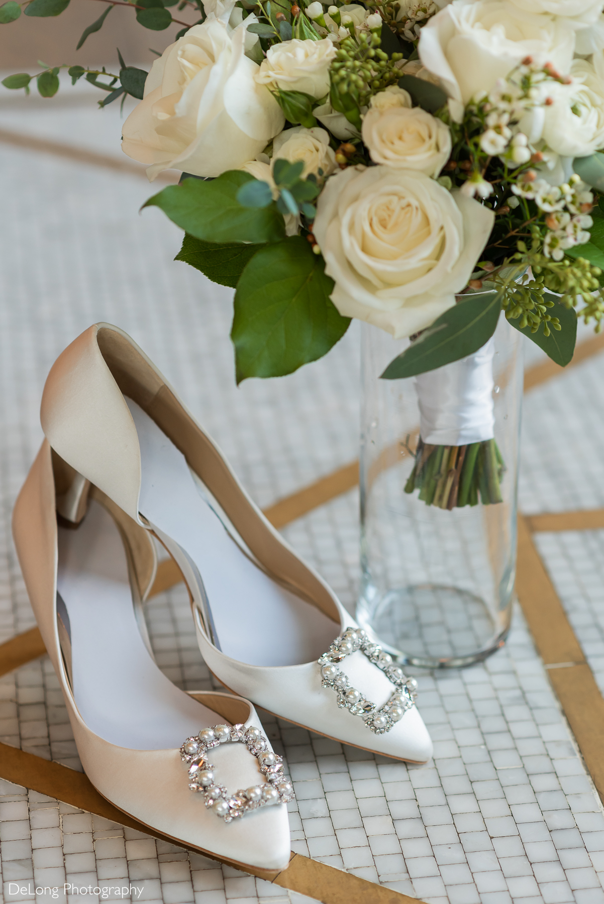 Bride's wedding bouquet featuring white roses next to her bedazzled white heels on an art deco marble floor with gold inlay. Photograph by Charlotte wedding photographers DeLong Photography taken in the Kimpton Hotel Arras.