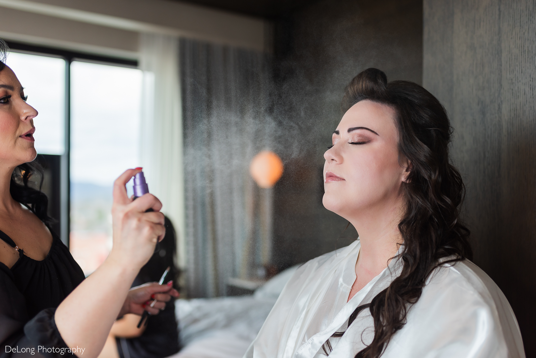 Bride being sprayed with makeup setting spray. You can see the droplets floating in the air. Photograph by Charlotte wedding photographers DeLong Photography taken in the Kimpton Hotel Arras.