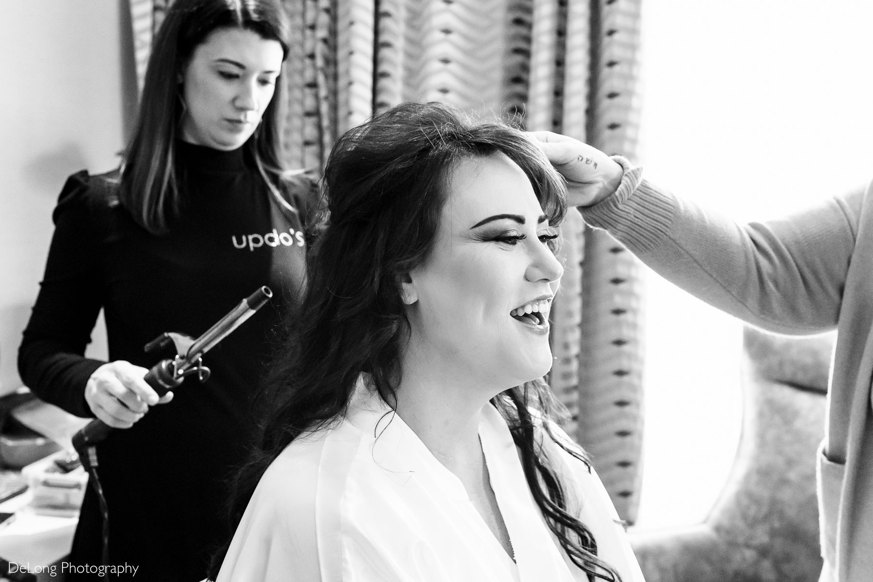 Black and white photograph of the bride laughing as she is getting her hair done. Photograph by Charlotte wedding photographers DeLong Photography taken in the Kimpton Hotel Arras.