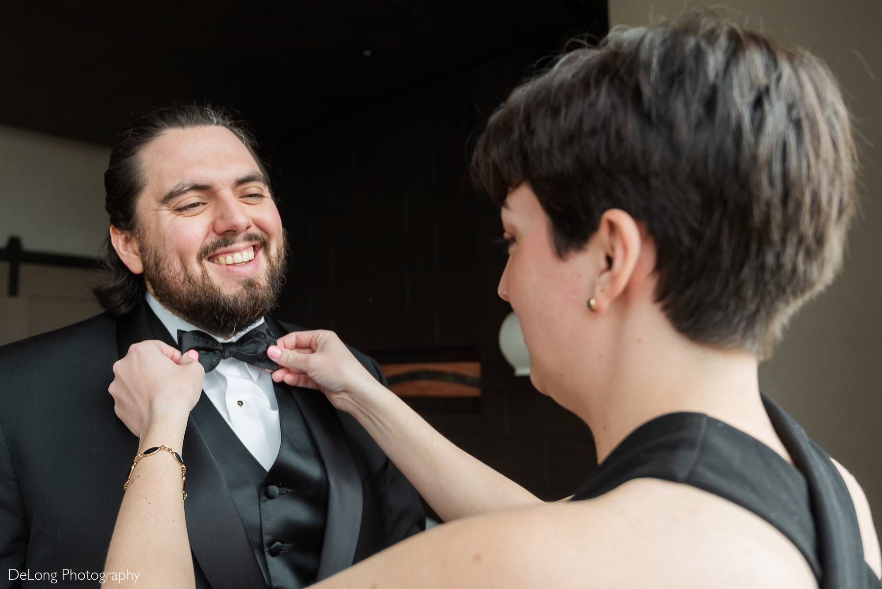 Groom smiling as his best persona adjusts his tie while getting ready. Photograph by Charlotte wedding photographers DeLong Photography taken in the Kimpton Hotel Arras.