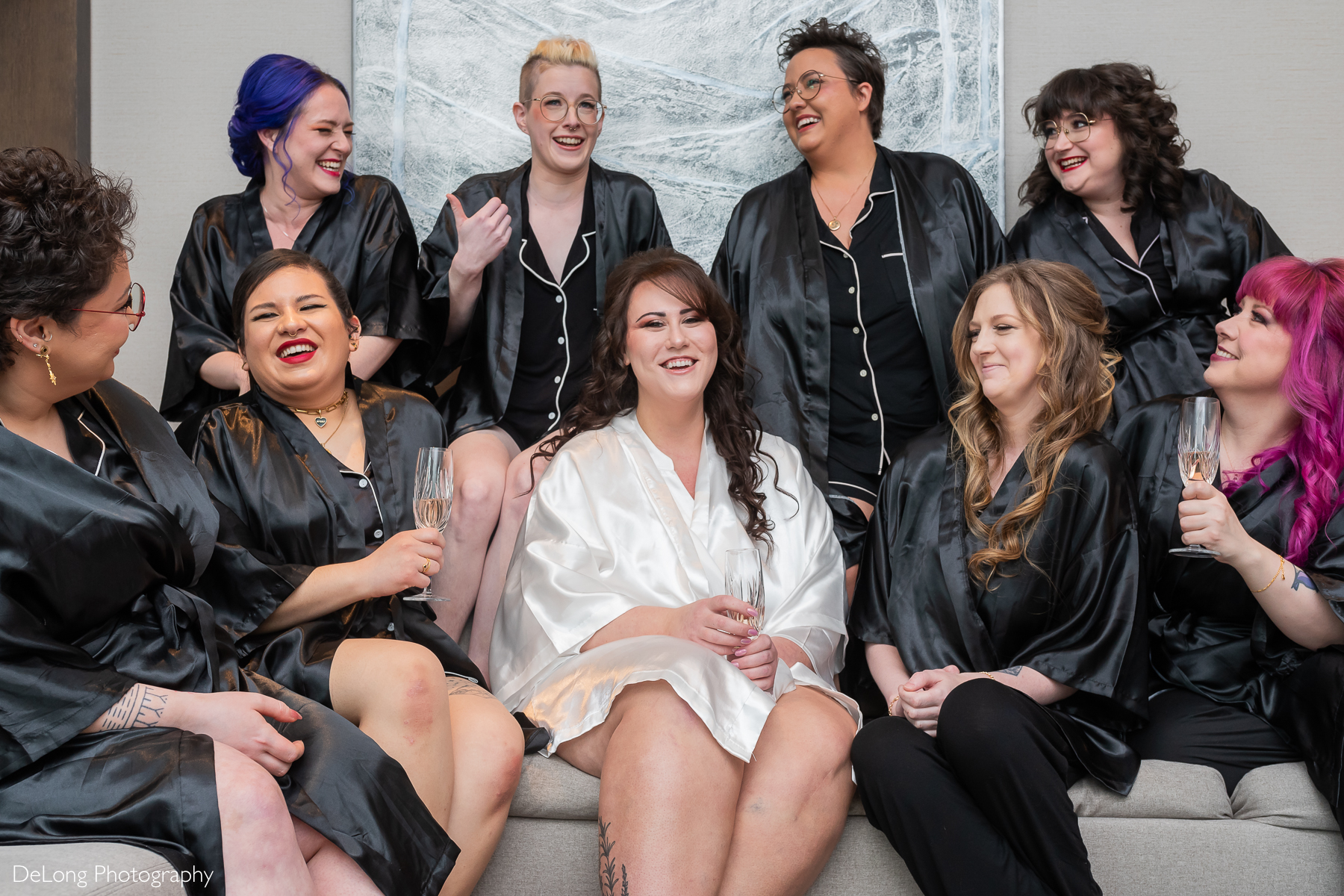 Bride laughing surrounded by her best friends on the sofa of her suite. Photograph by Charlotte wedding photographers DeLong Photography taken in the Kimpton Hotel Arras.