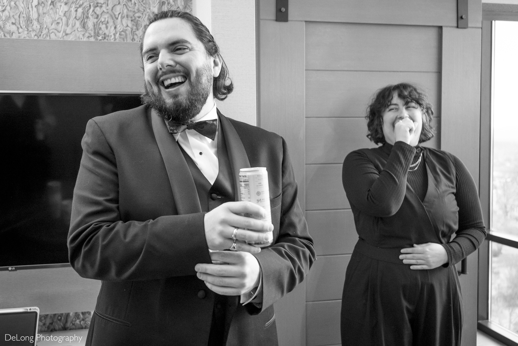 Black and white image of the groom and one of his groom's party laughing during the getting ready portion of the day. Photograph by Charlotte wedding photographers DeLong Photography taken in the Kimpton Hotel Arras.