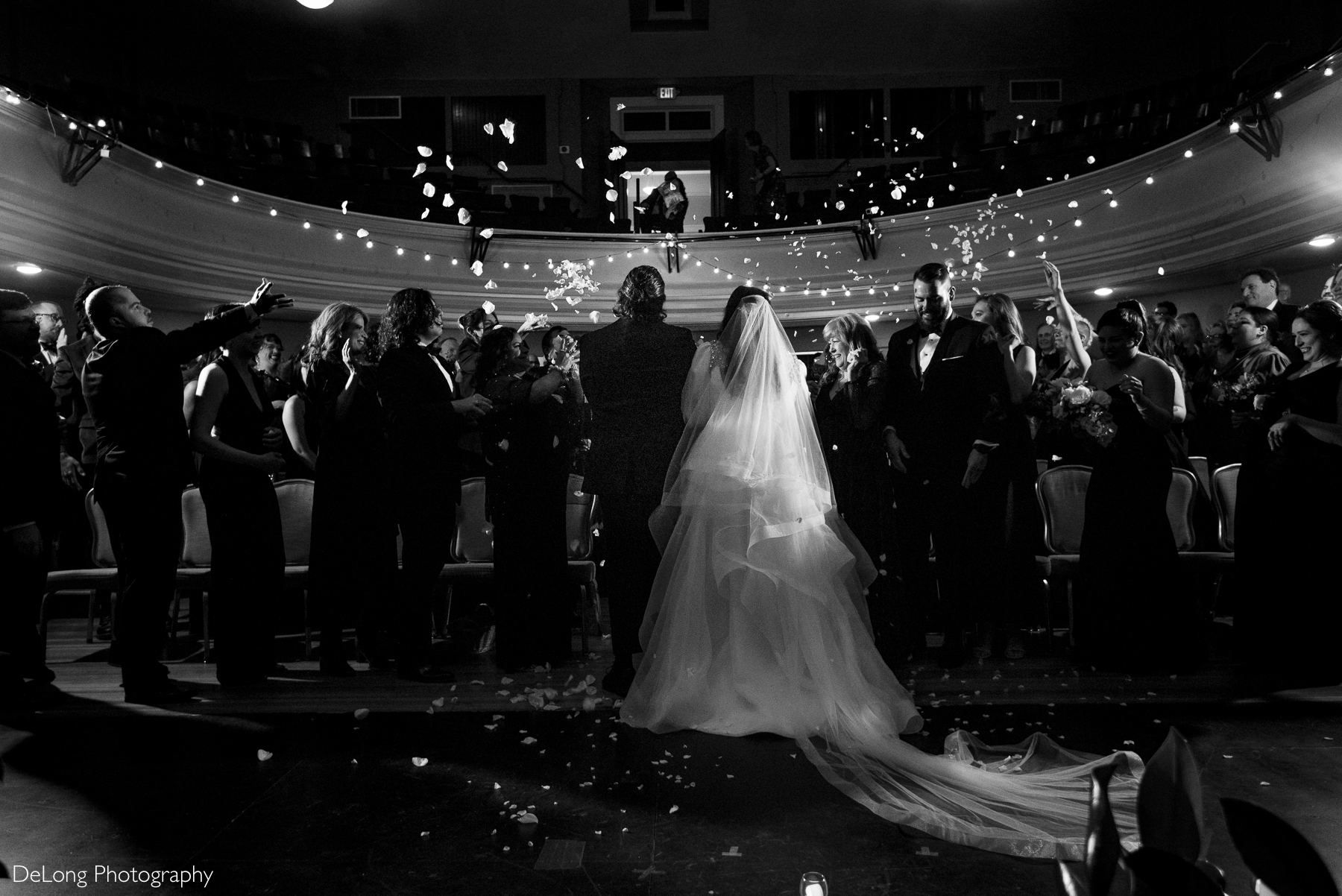 Black and white photograph of the bride and groom recessing down the aisle as flower petals are tossed in the air in celebration.Photograph by Charlotte wedding photographers DeLong Photography taken at the Asheville Masonic Temple.