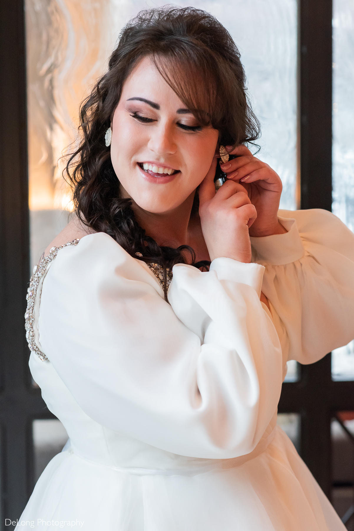 Bride gigling while putting on her earrings. Photograph by Charlotte wedding photographers DeLong Photography taken in the Kimpton Hotel Arras.