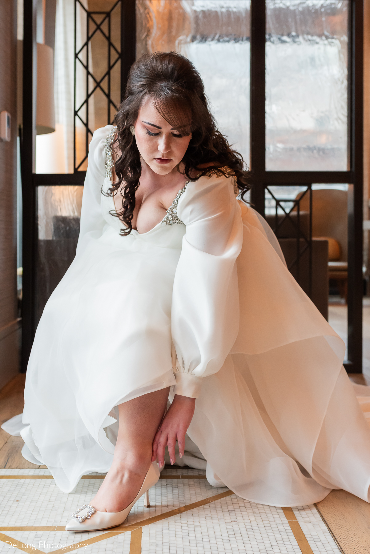 Bride reaching down and adjusting high-heels. Photograph by Charlotte wedding photographers DeLong Photography taken in the Kimpton Hotel Arras.