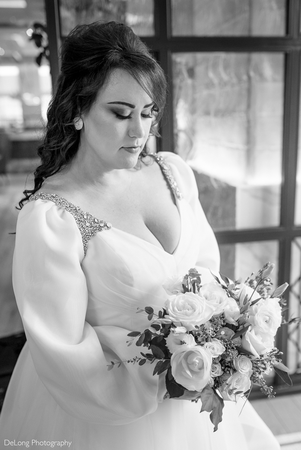 Black and white portrait of the bride looking down at her bouquet. The image highlights the bride's eye makeup and top of her dress. Photograph by Charlotte wedding photographers DeLong Photography taken in the Kimpton Hotel Arras.