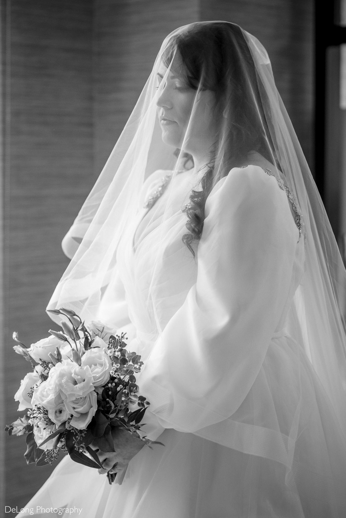 Black and white ethereal portrait of the bride under her vail looking downward toward her bouquet. Photograph by Charlotte wedding photographers DeLong Photography taken in the Kimpton Hotel Arras.