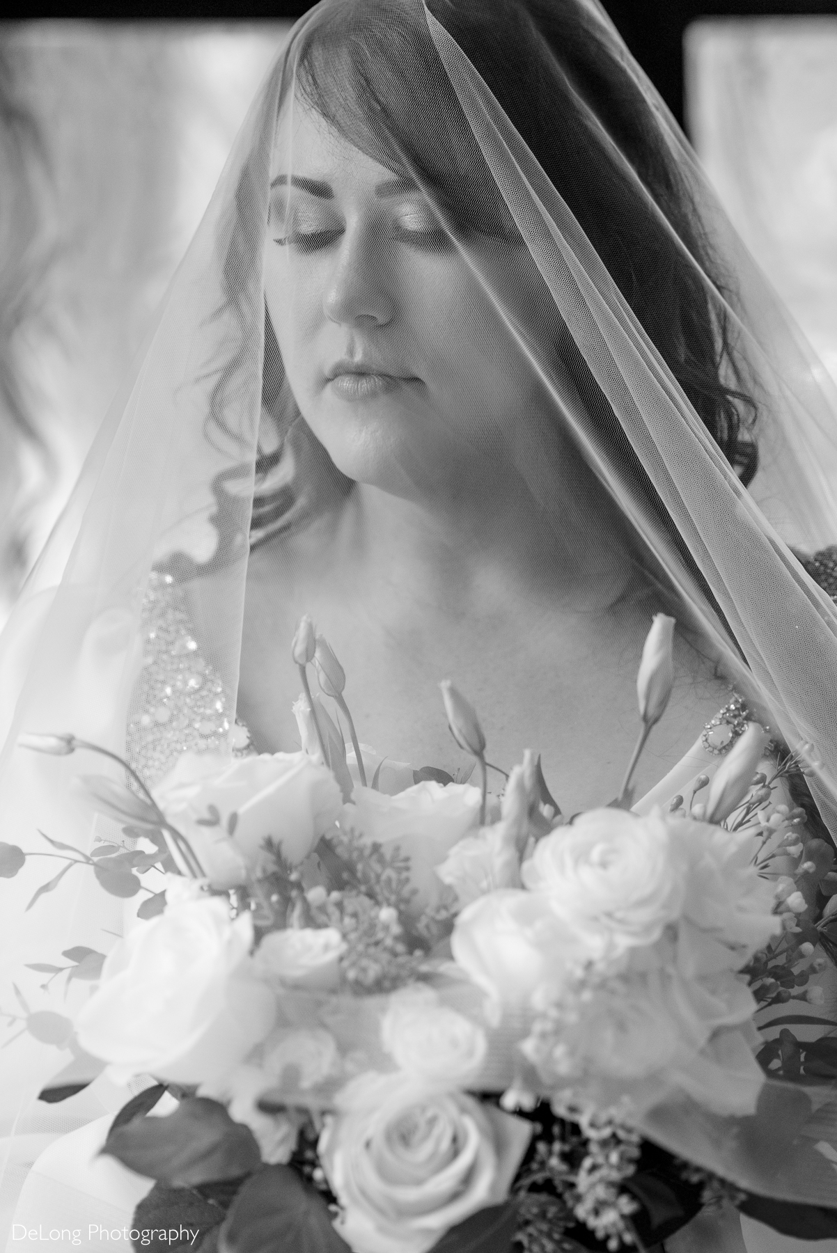 Black and white close portrait of the bride with the vail cascading over her. Her bouquet is shown in the bottom of the frame. Photograph by Charlotte wedding photographers DeLong Photography taken in the Kimpton Hotel Arras.