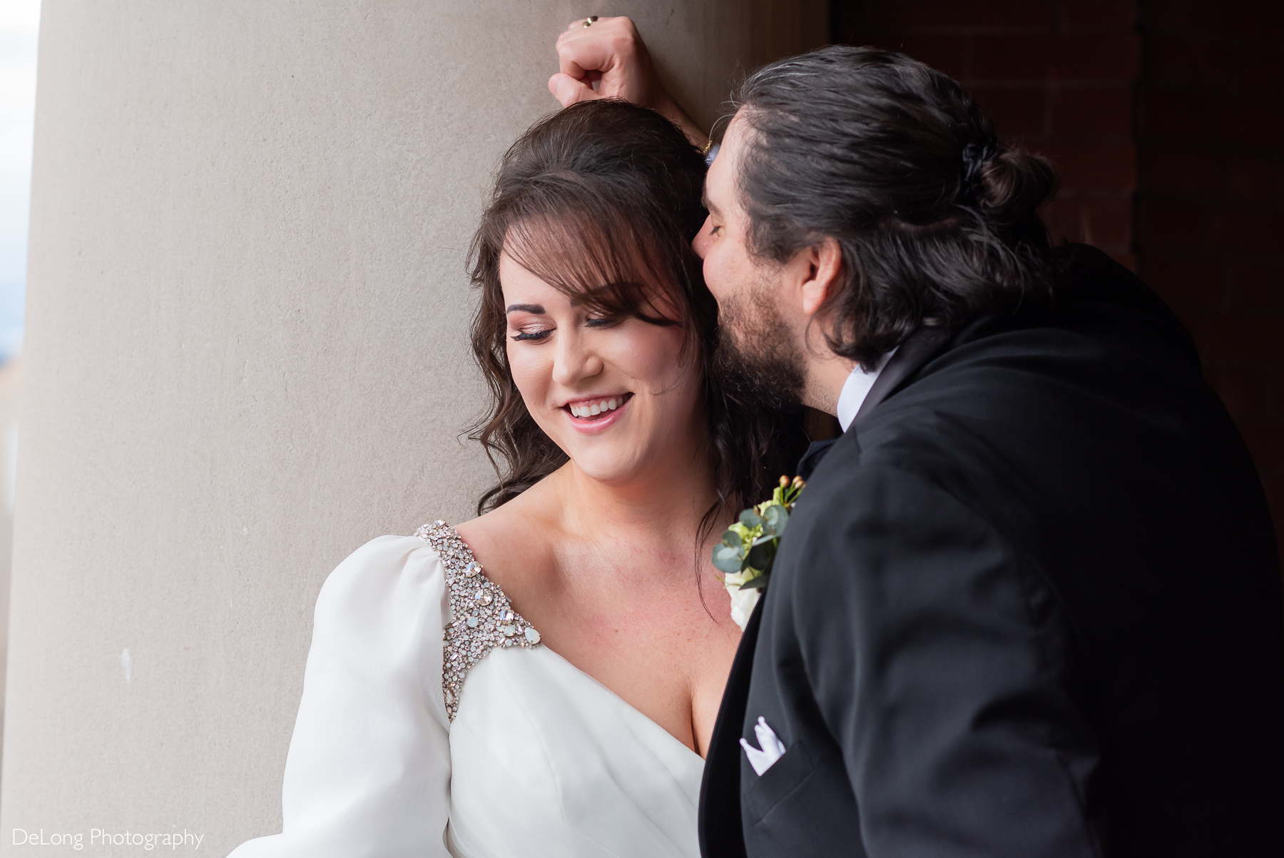 Bride smiling and looking down as the groom whispers in her ear. Photograph by Charlotte wedding photographers DeLong Photography taken at the Asheville Masonic Temple.