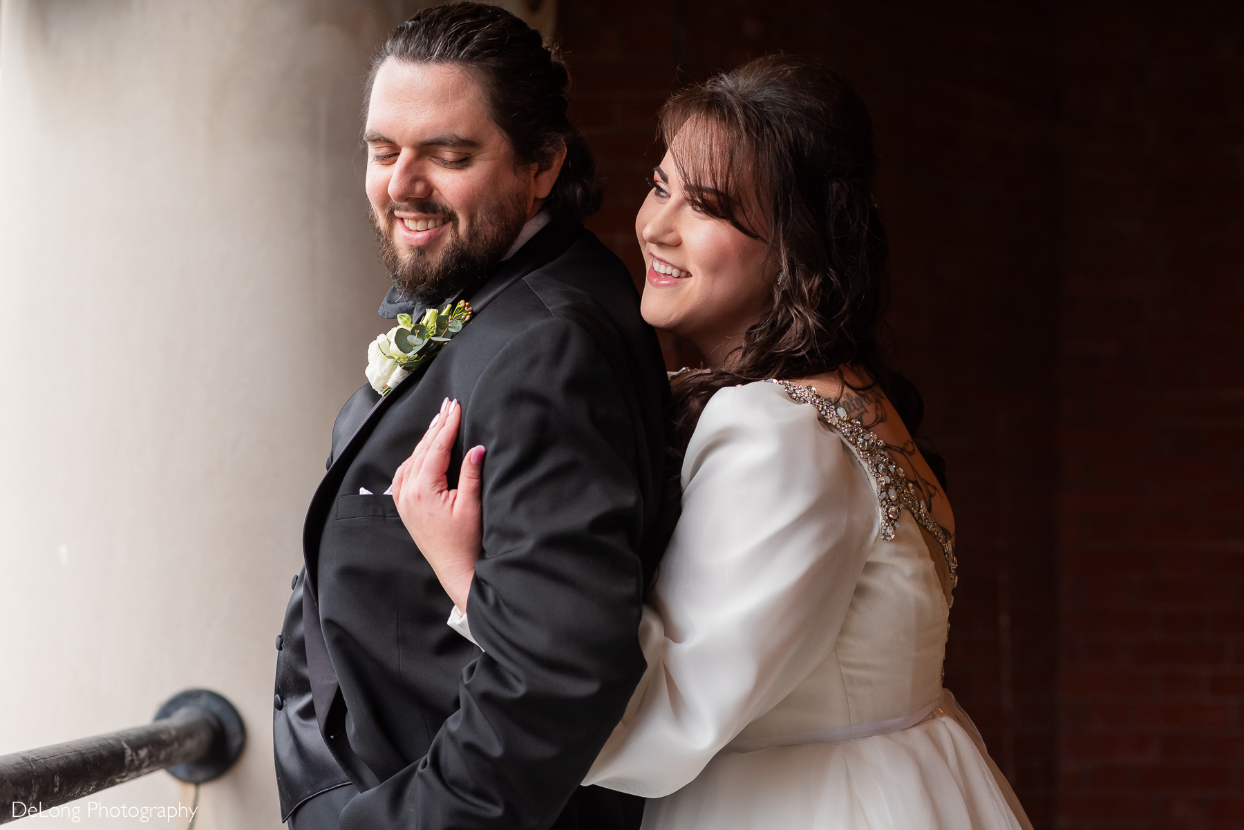 Bride hugging her groom from behind. He is looking back toward her. They are both smiling. Photograph by Charlotte wedding photographers DeLong Photography taken at the Asheville Masonic Temple.