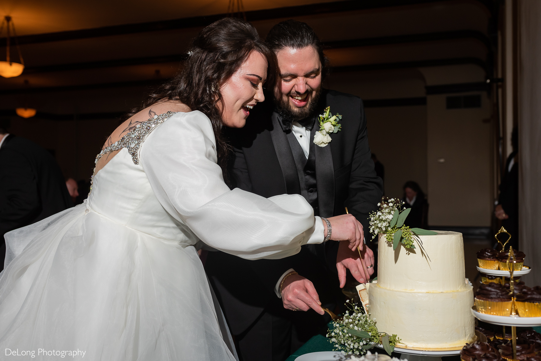 Bride and groom laughing as they cut their wedding cake. Photograph by Charlotte wedding photographers DeLong Photography taken at the Asheville Masonic Temple.