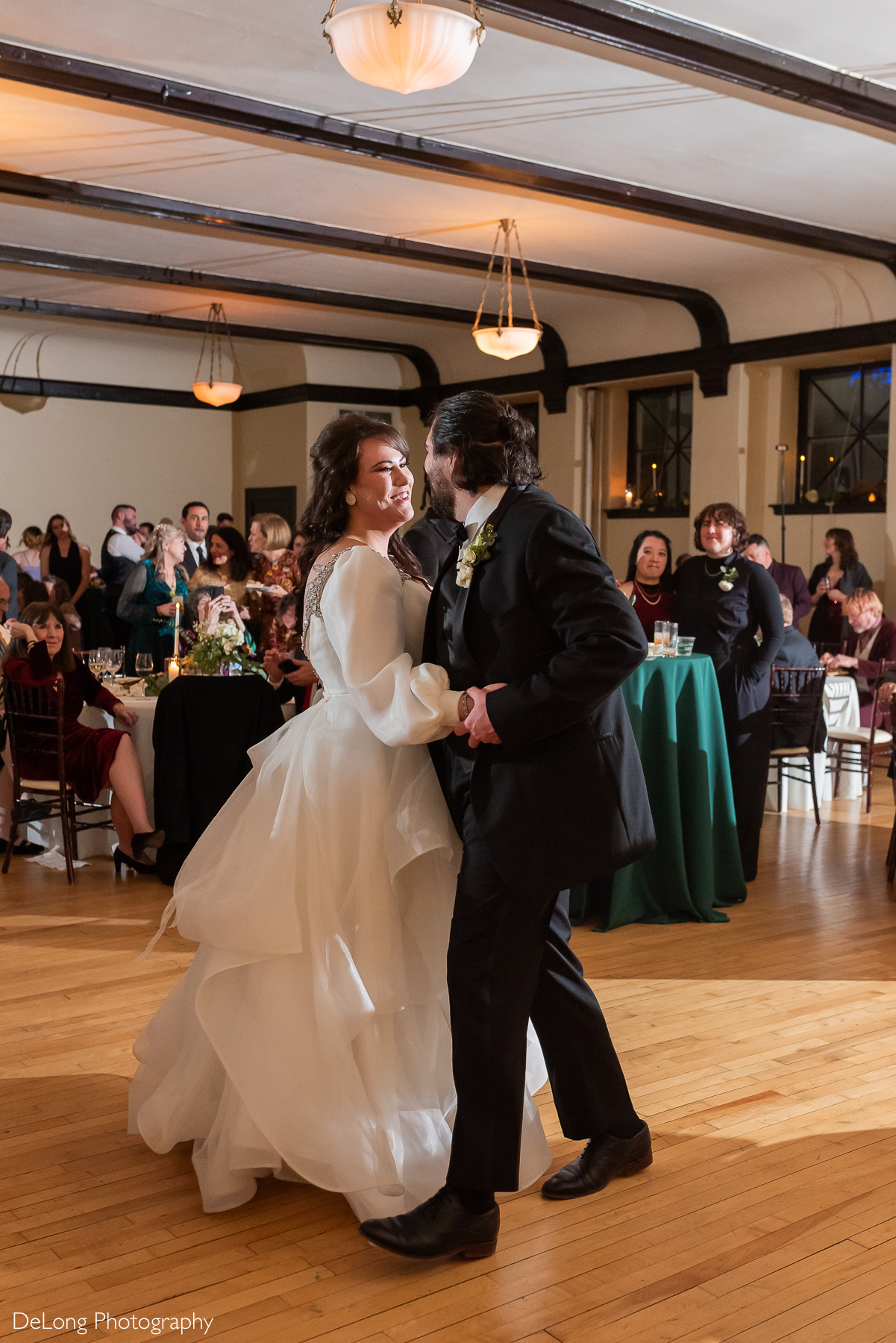 Bride and groom smiling at one another as their entertain guests with their choreographed dance. Photograph by Charlotte wedding photographers DeLong Photography taken at the Asheville Masonic Temple.