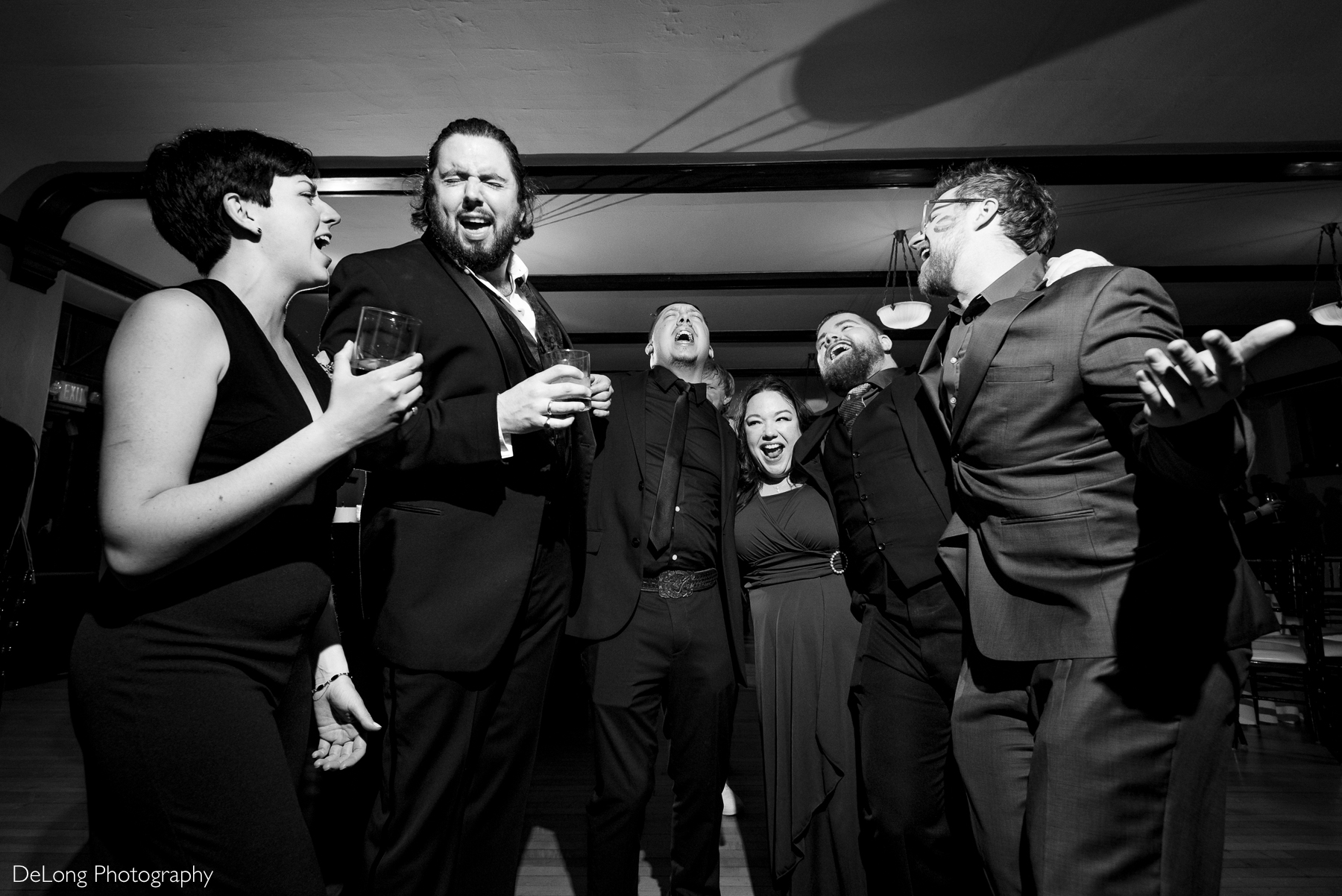 Black and white photograph of the groom and some of his friends belting out lyrics to a favorite song.Photograph by Charlotte wedding photographers DeLong Photography taken at the Asheville Masonic Temple.