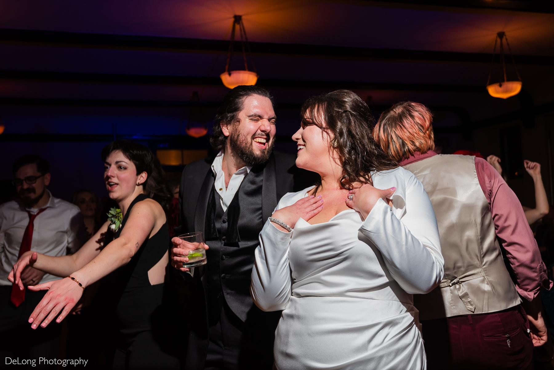 Bride and groom laughing at one another on the crowded dance floor. Photograph by Charlotte wedding photographers DeLong Photography taken at the Asheville Masonic Temple.