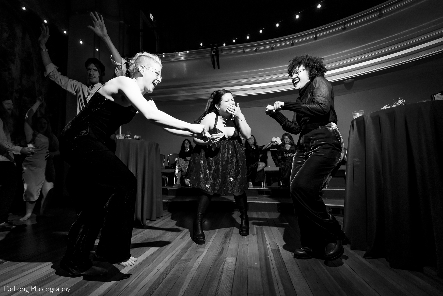 Black and white photograph of 3 girls cracking up laughing and dancing with one another at the after-party. Photograph by Charlotte wedding photographers DeLong Photography taken at the Asheville Masonic Temple.