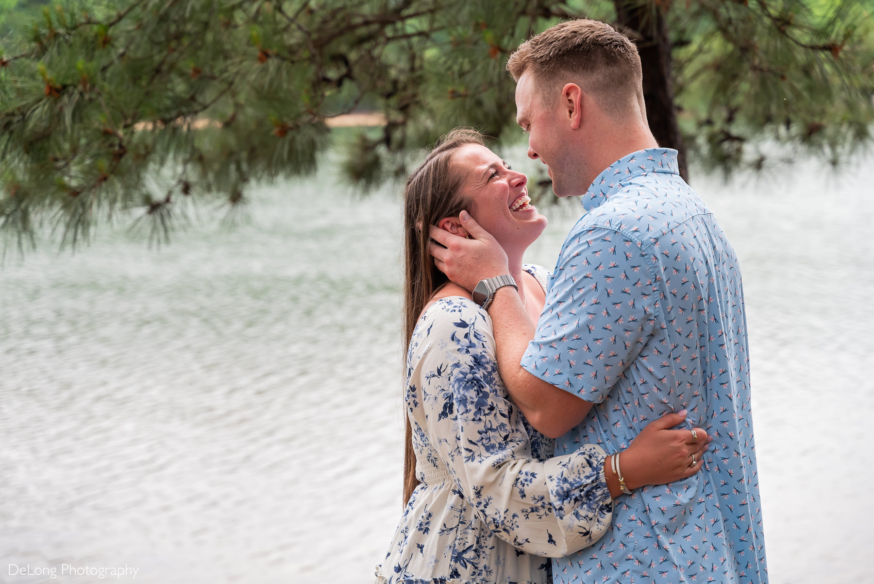 Woman smiling as man holds both sides of her face. They are looking into each others eyes sharing the joy of just becoming engaged. 